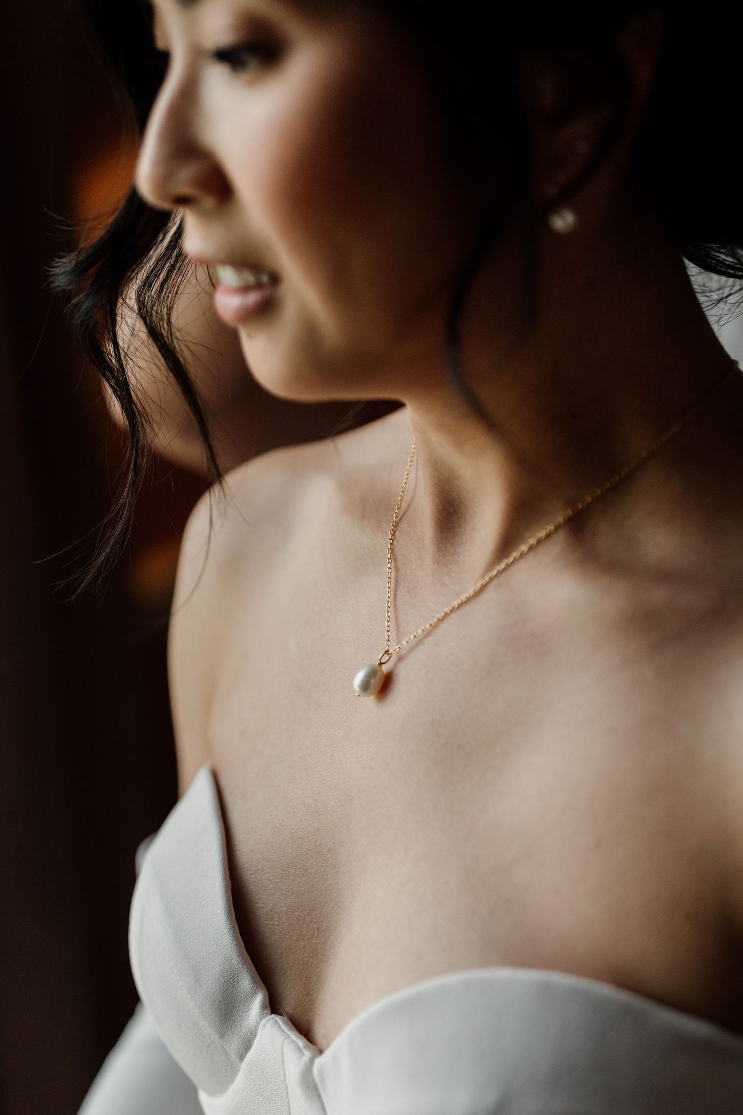 Close-up shot of delicate gold necklace around a neck with a white dress in soft lighting.