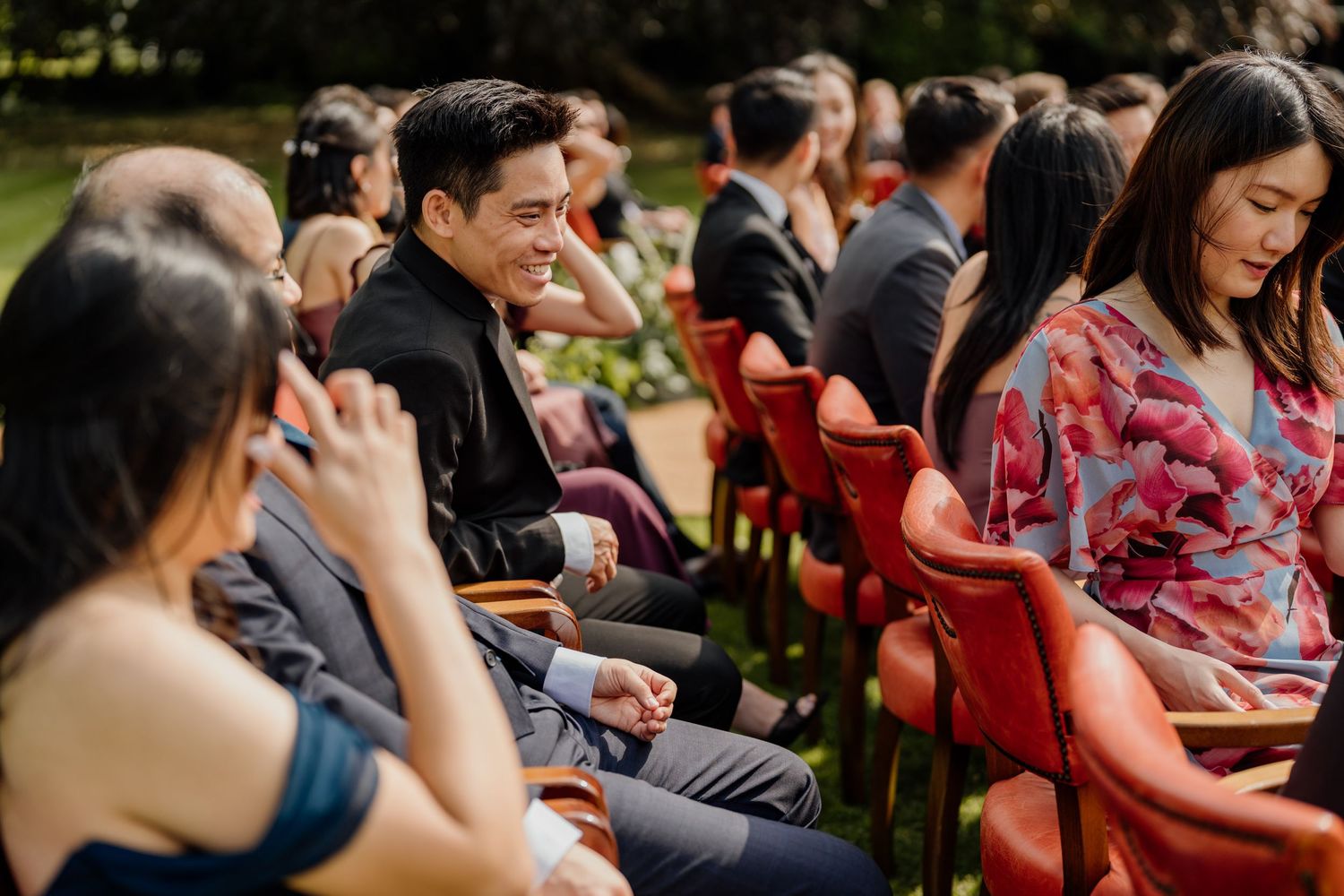 Wedding guests smile and react emotionally during an outdoor ceremony.