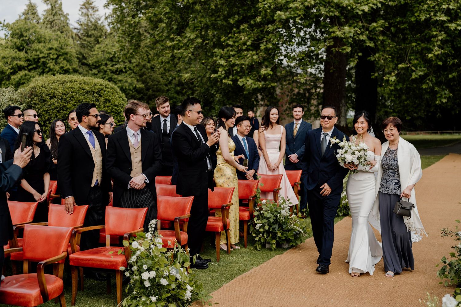 Garden wedding ceremony setup with red chairs arranged in rows on a manicured lawn.