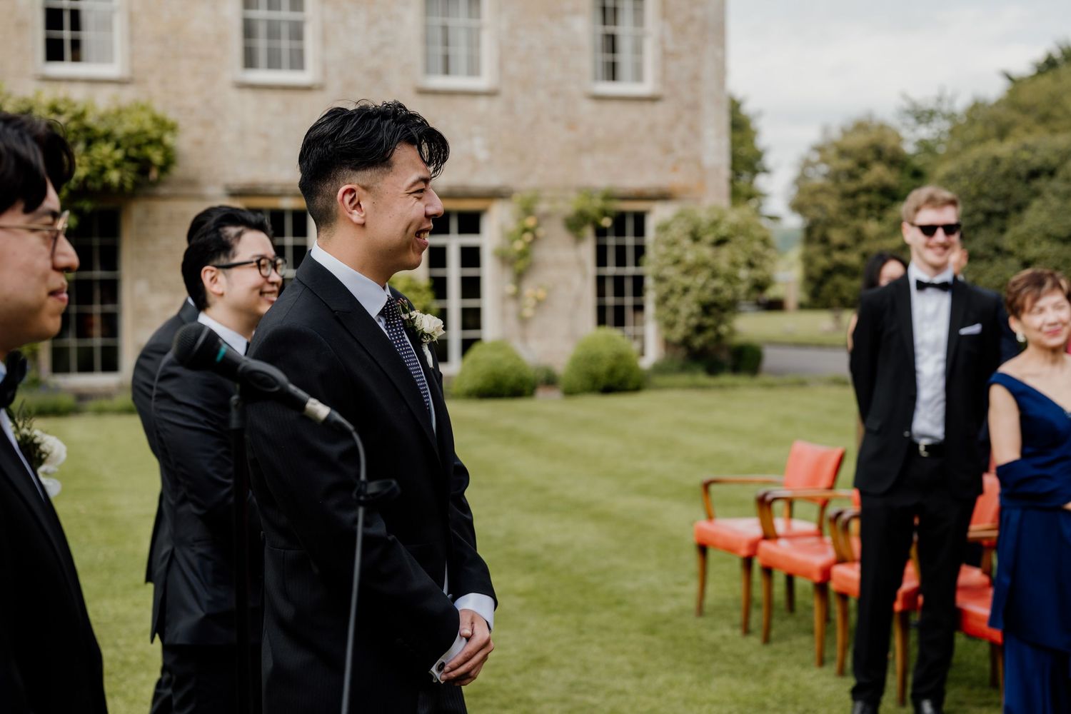Wedding guests mingle on the lawn of an elegant stone country estate during an outdoor celebration.
