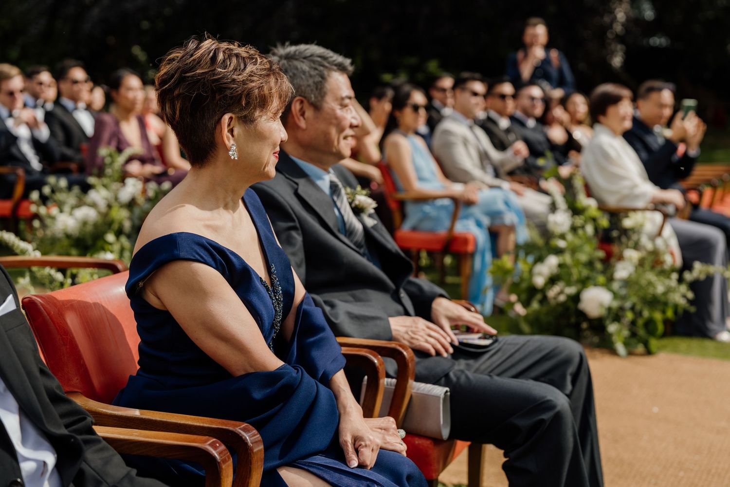 Outdoor wedding ceremony seating arrangement with wooden chairs and guests in attendance.