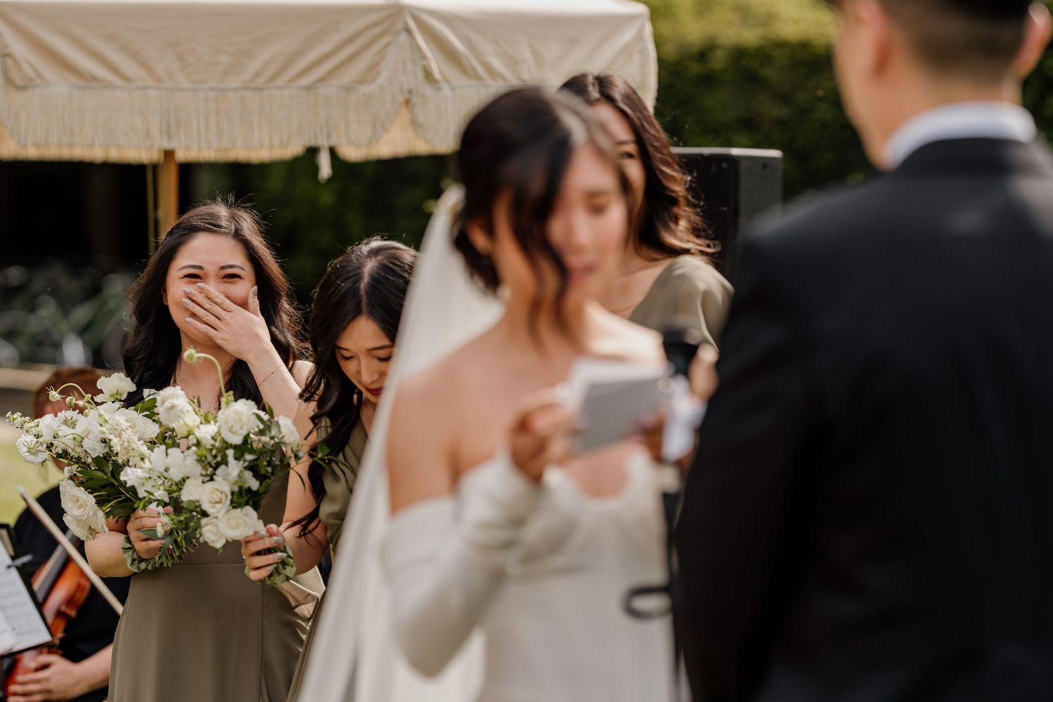 Wedding party and guests celebrating during an outdoor reception under white tent.