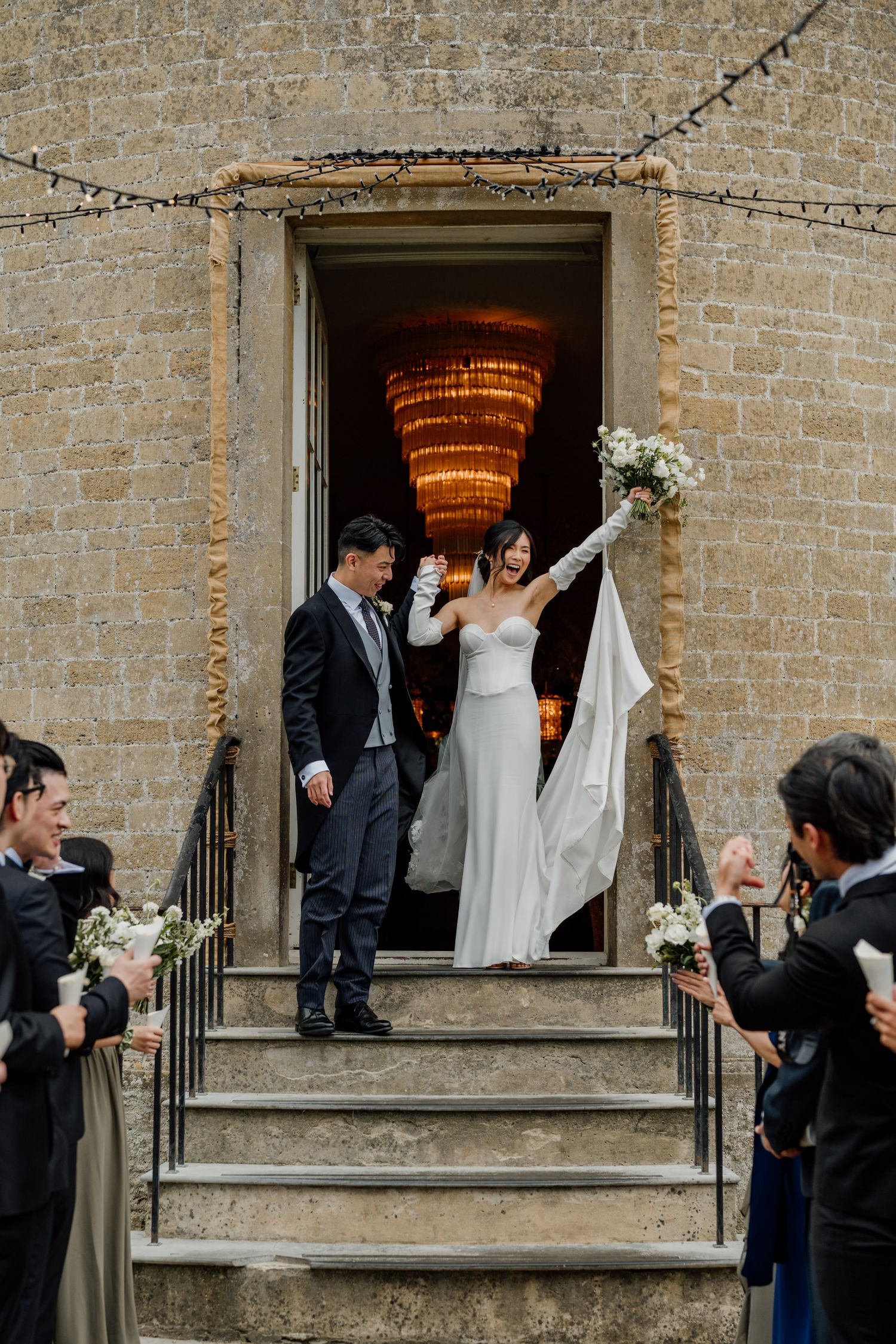 Wedding celebration outside a historic stone building with string lights and elegant decor.