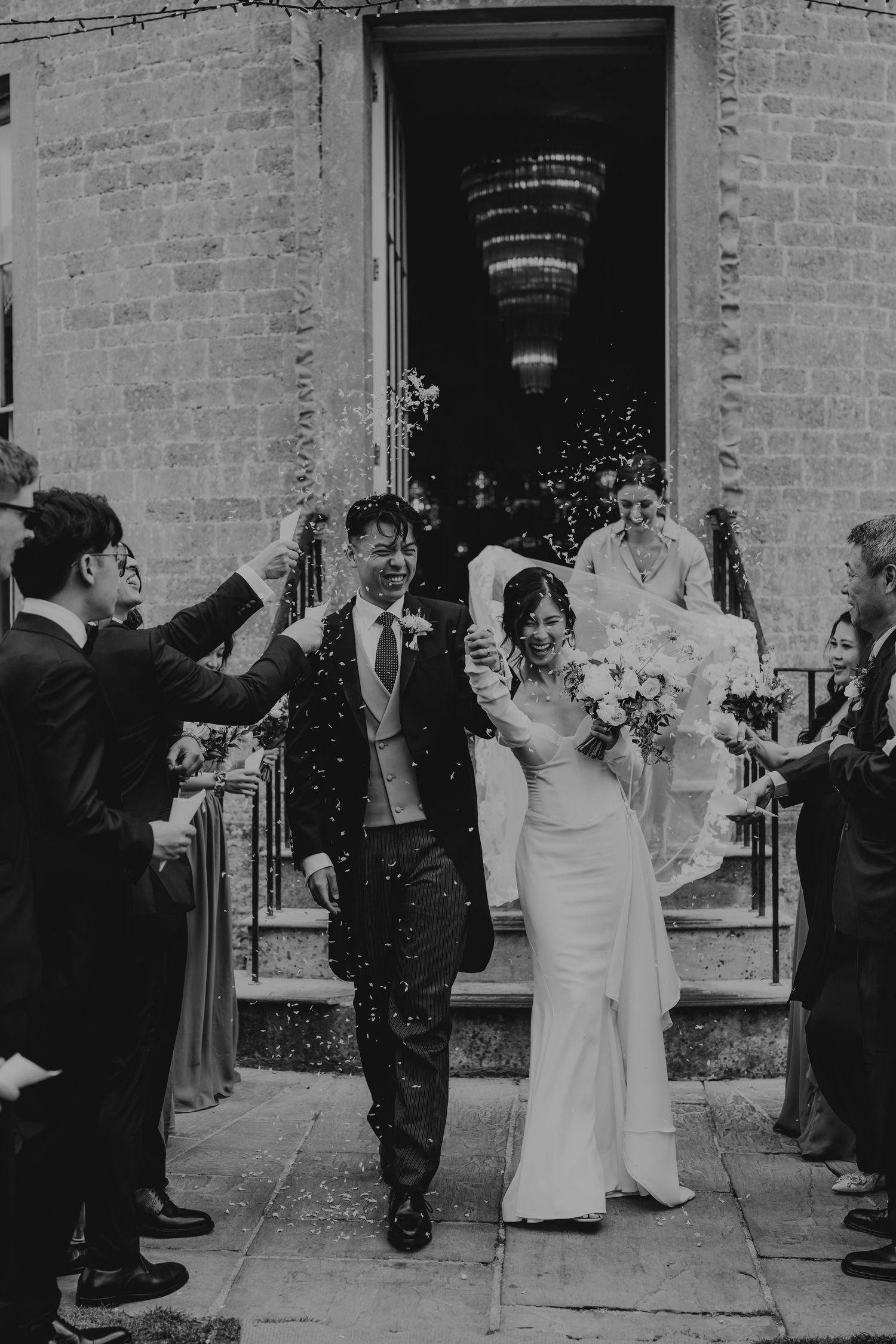 Wedding exit celebration with guests throwing confetti outside a historic brick building.