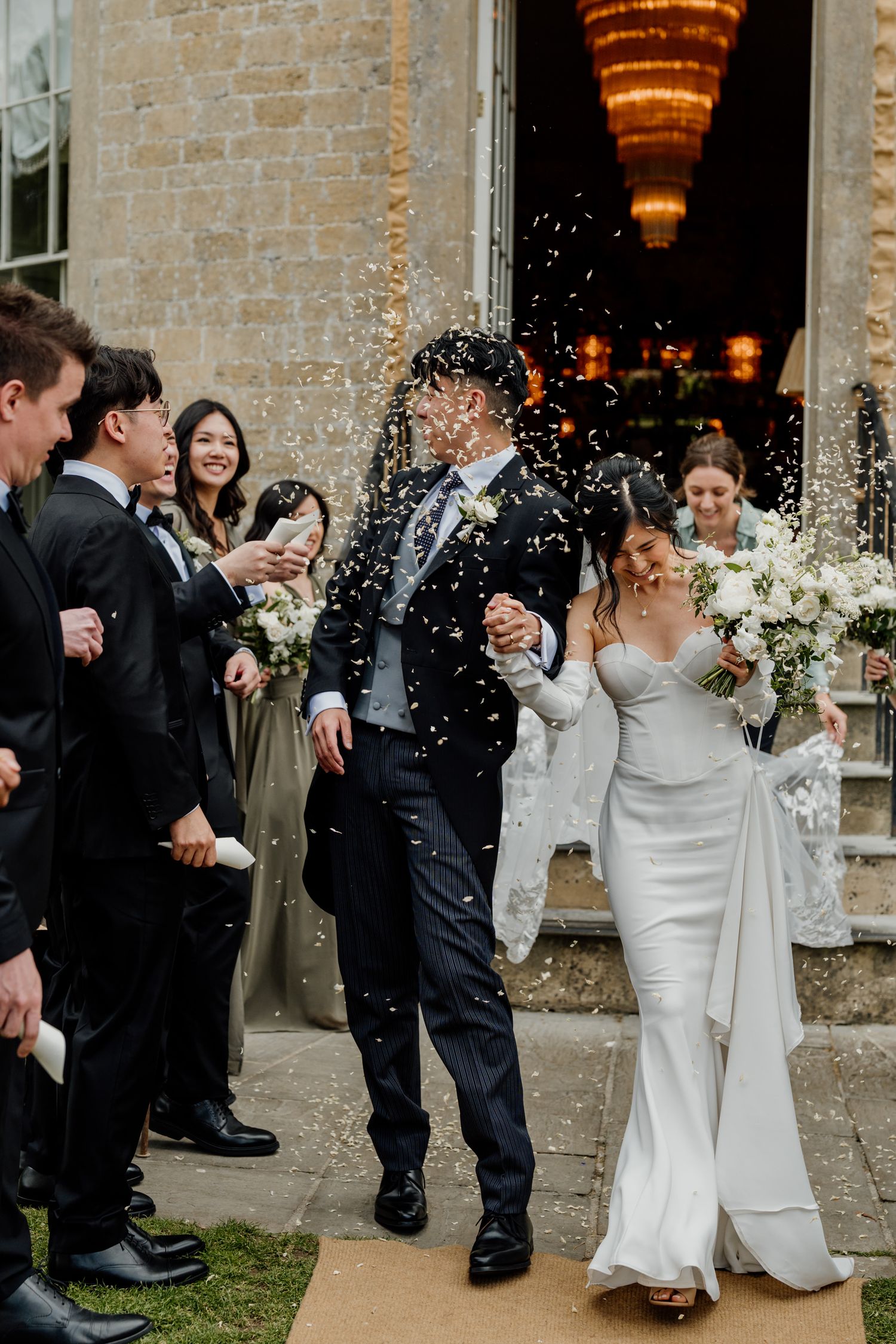 Wedding celebration with confetti being thrown outside a grand stone building with warm glowing lights.