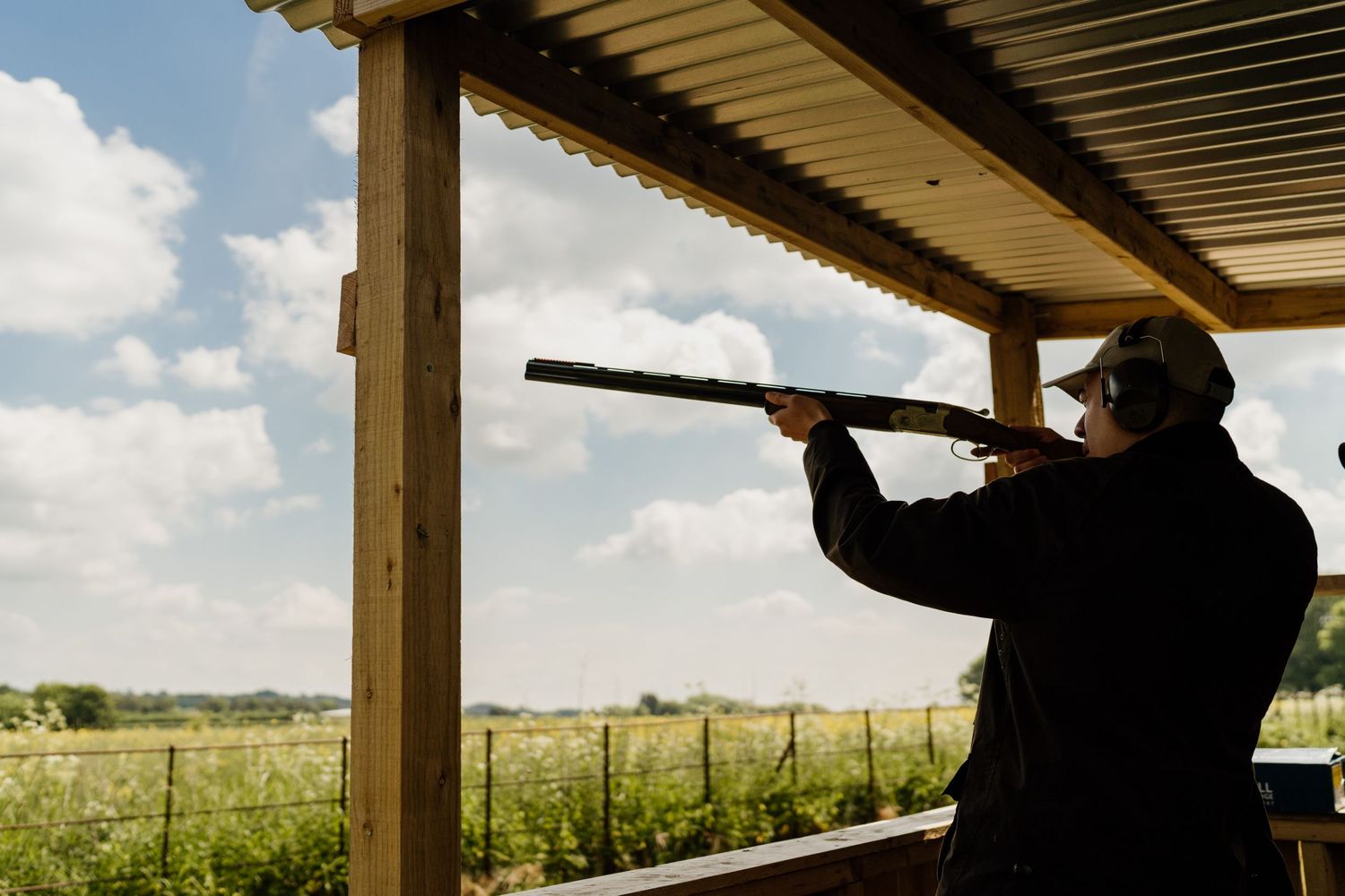 Silhouetted figure shooting with camera under covered porch with rural landscape background.