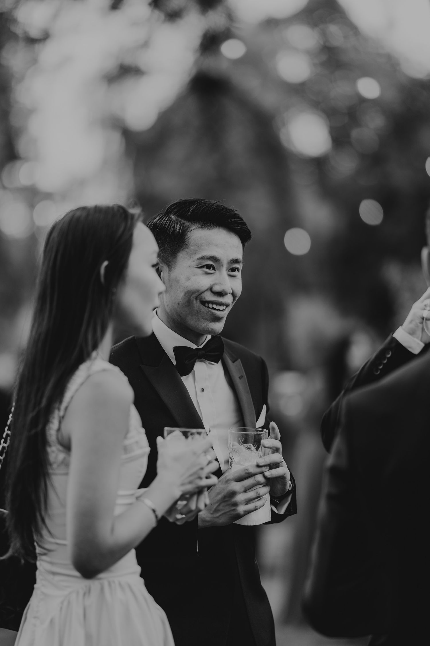 Black and white photo of wedding guests laughing and socializing at a reception celebration.