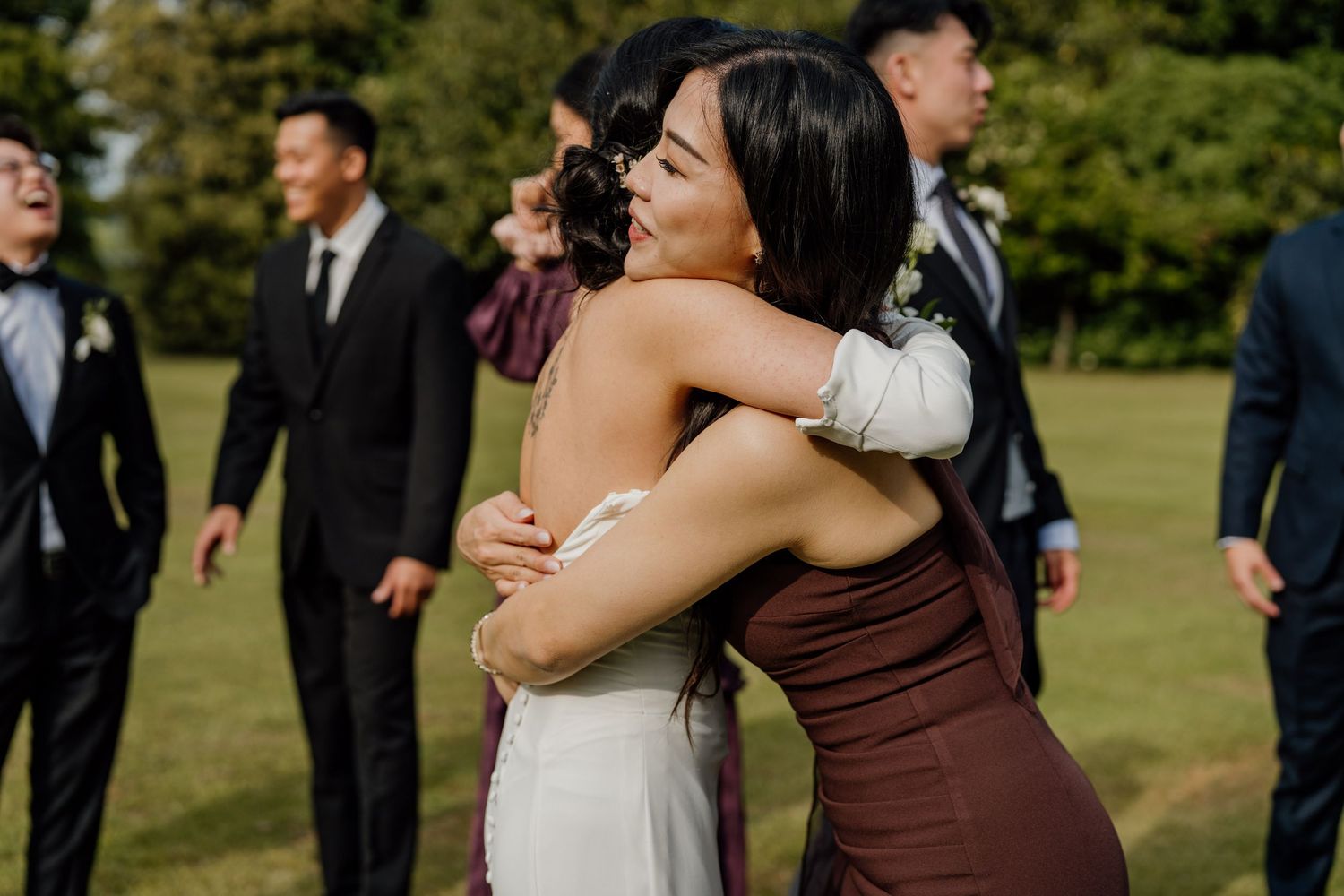 Wedding party gathered on green lawn during outdoor celebration with people hugging and embracing.