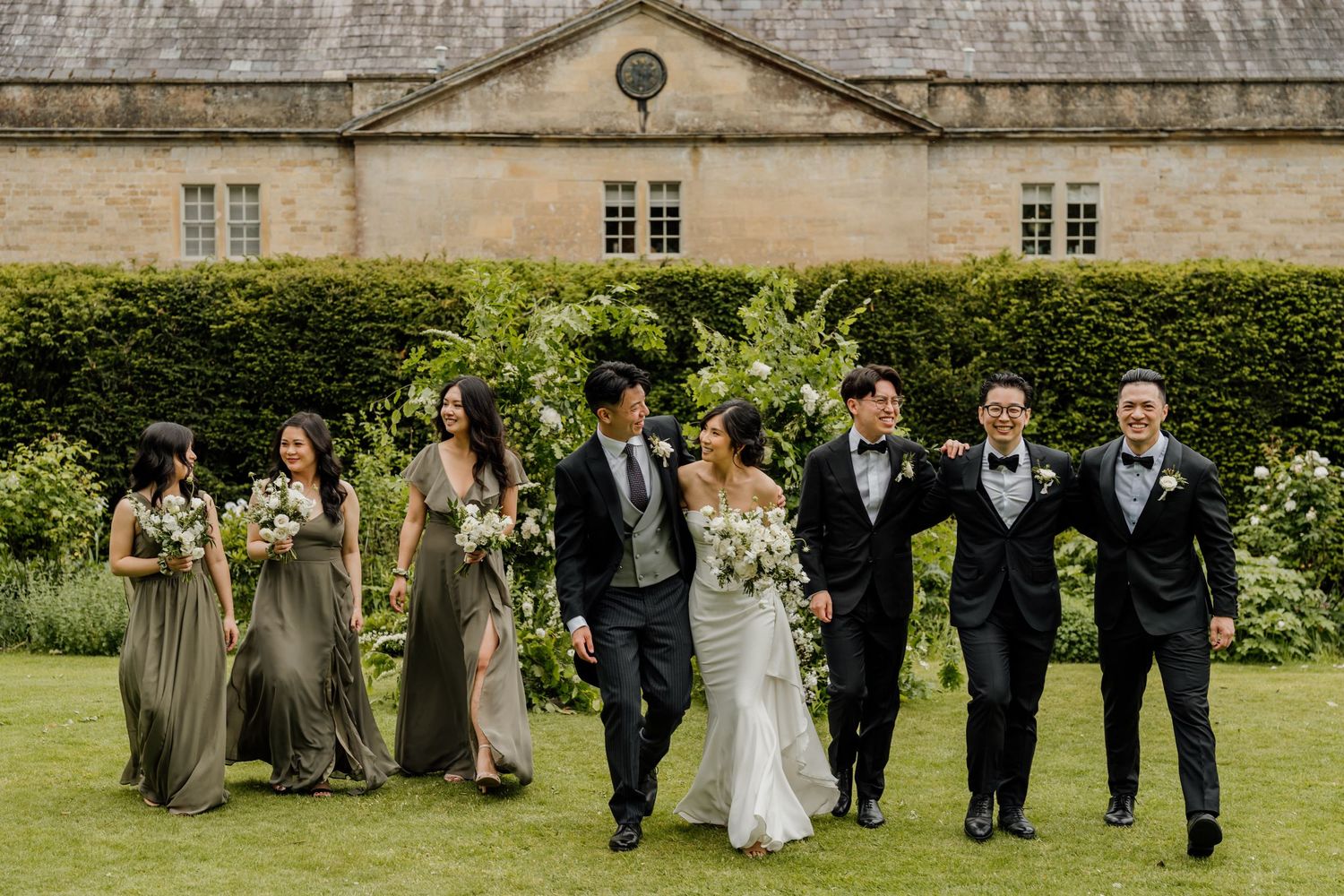 Wedding party walking together through a garden setting with lush greenery in the background.