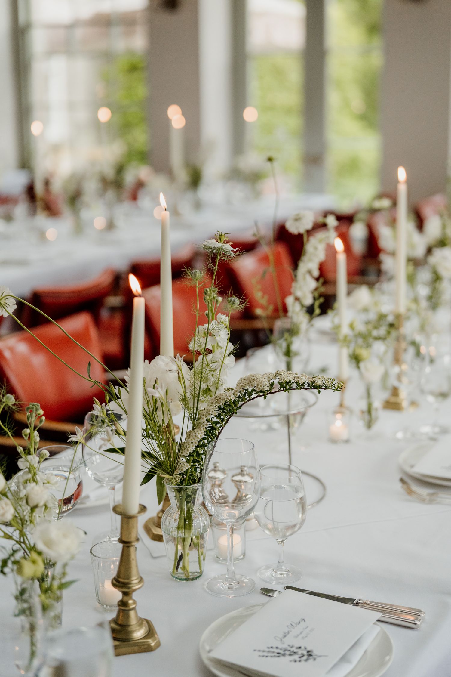 Elegant wedding reception table with white linens, taper candles, and delicate floral centerpieces in glass vases.