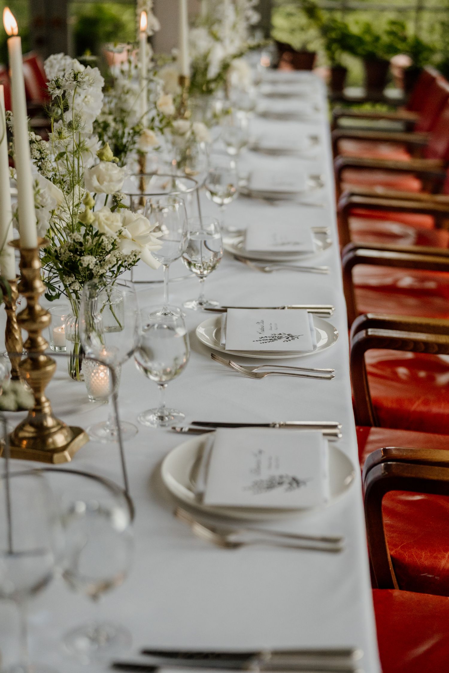 Elegant wedding reception table setting with white linens, red chairs and delicate floral centerpieces.