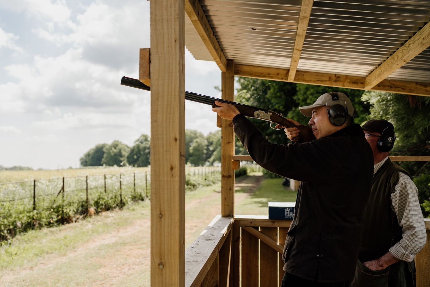 Clay pigeon shooter takes aim at target from wooden shooting platform.