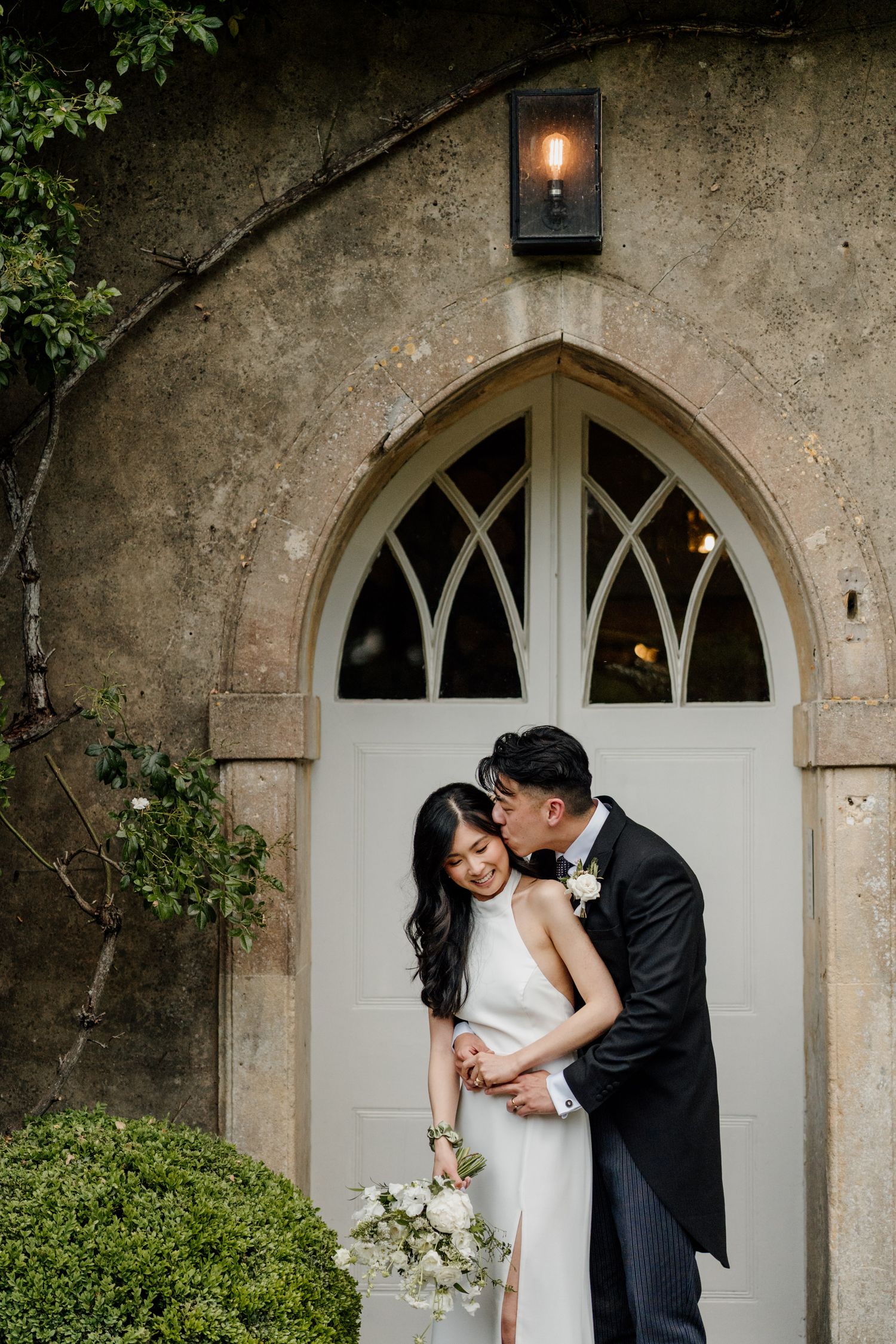 Wedding couple shares intimate moments in front of an elegant arched doorway of a historic stone building.