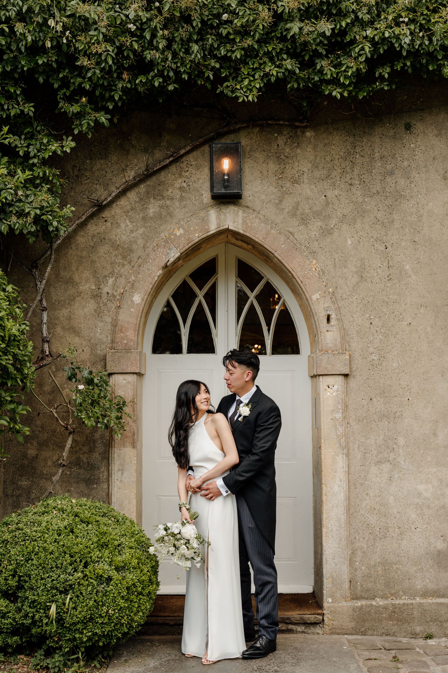 Romantic wedding portraits of a couple posing near an arched doorway on their special day.