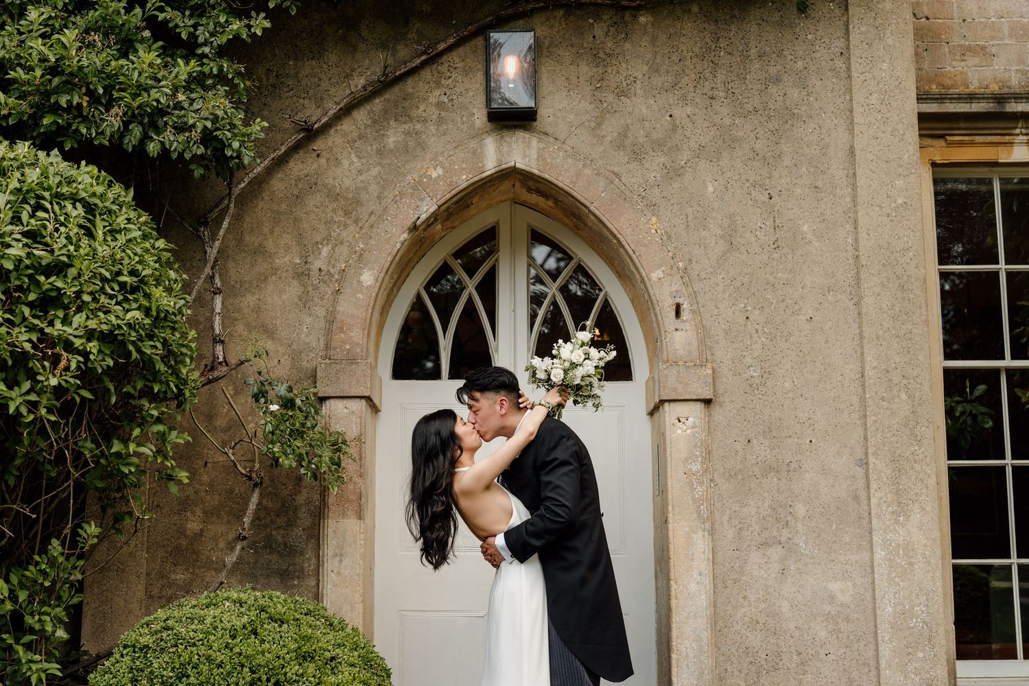 Happy couple embraces and poses against stone architecture during sunset wedding photography session.