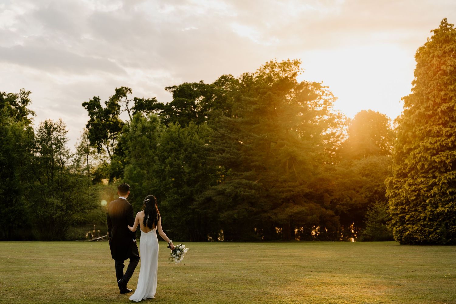 Golden sunset light illuminates wedding photos on grassy field.