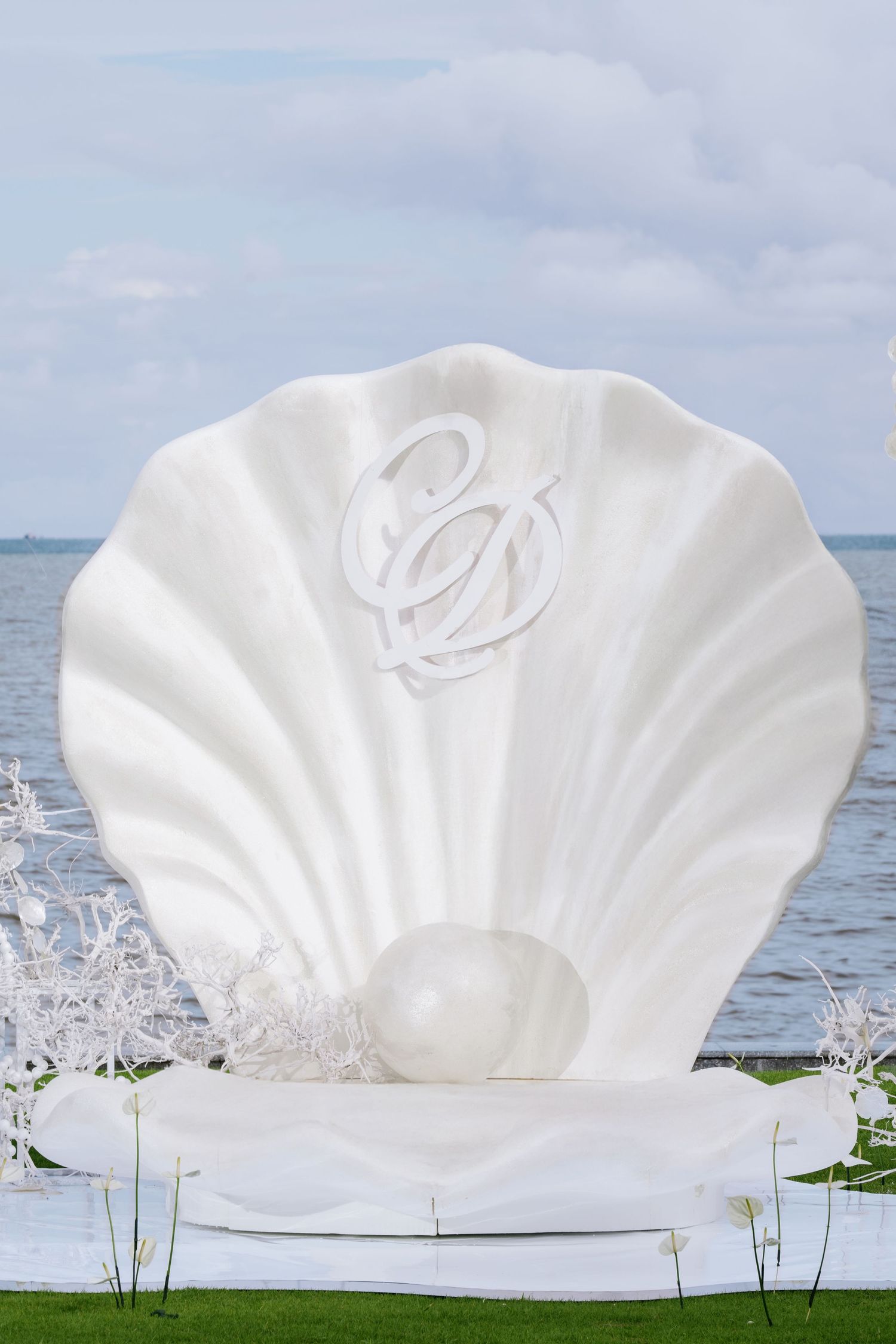 Giant white scallop shell wedding ceremony backdrop with monogram and pearl detail by the ocean.