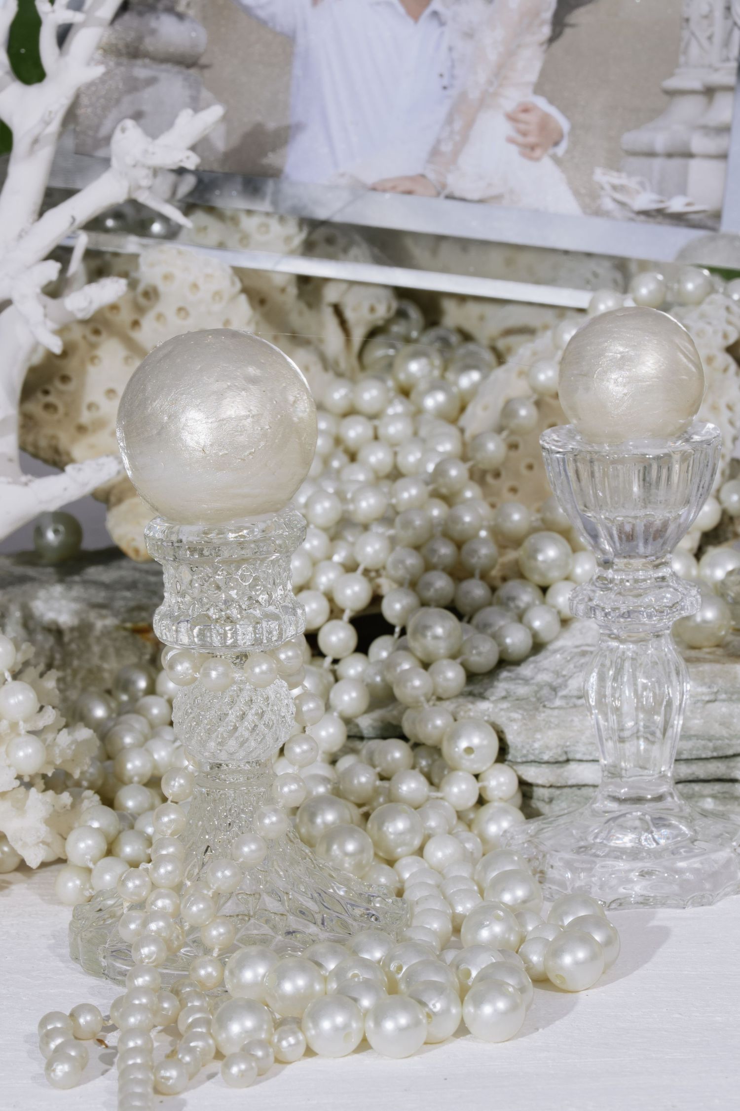 Crystal candleholders with pearl sphere toppers surrounded by white pearl bead strands and wedding photo display.