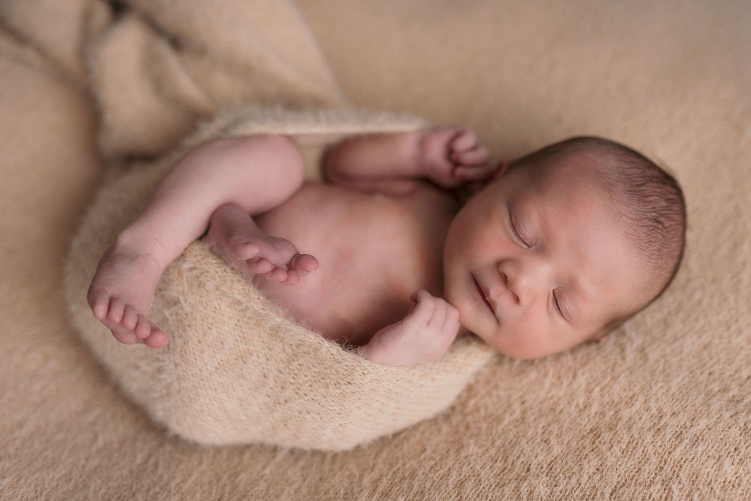 Peaceful newborn sleeping on soft beige blanket with delicate features.