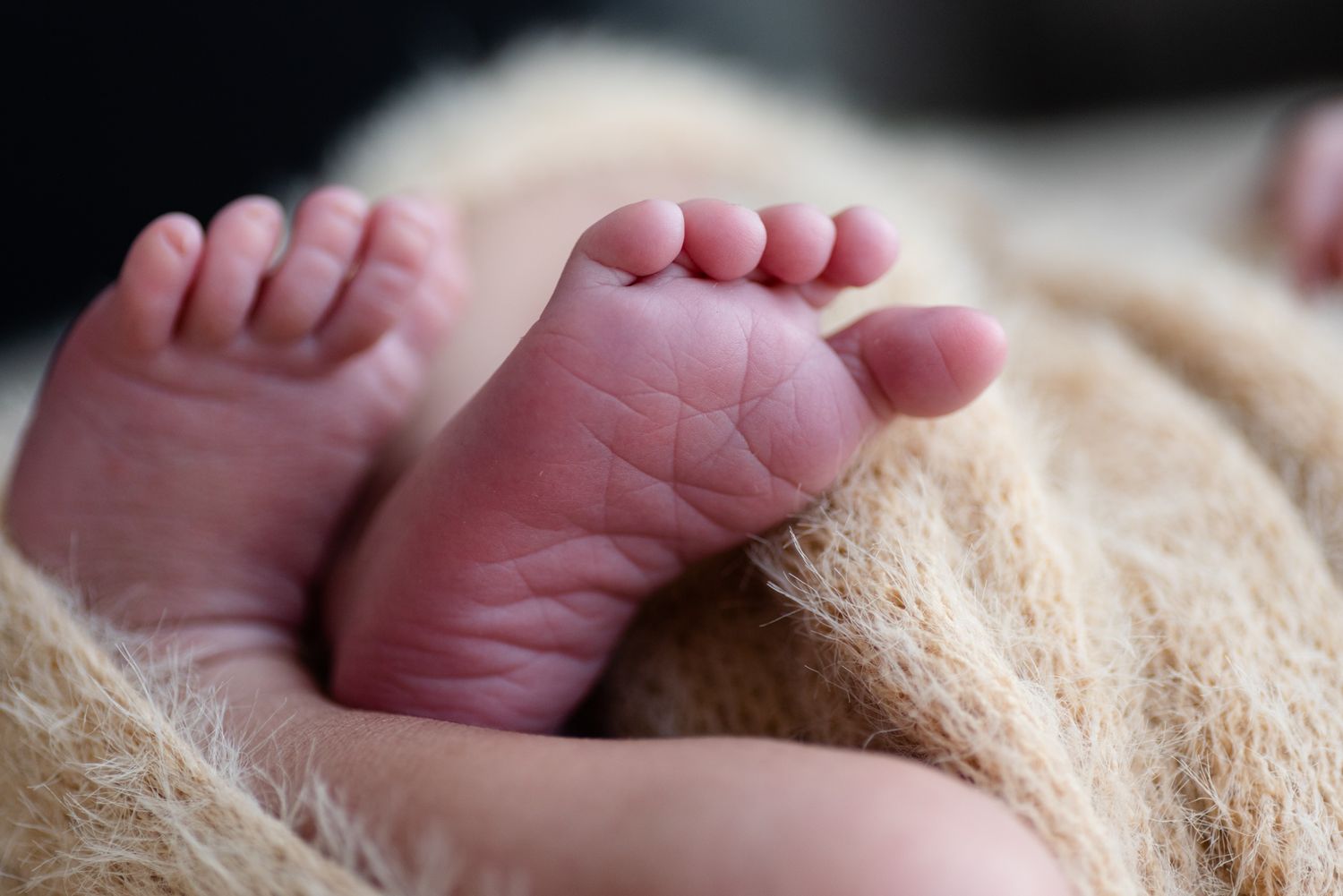 Tiny newborn feet with wrinkled soles rest on a cream-colored textured blanket.