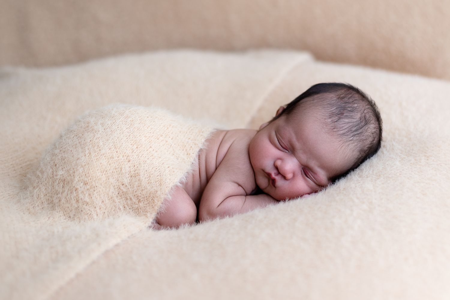 Sleeping newborn nestled in soft beige bedding during a professional photo session.