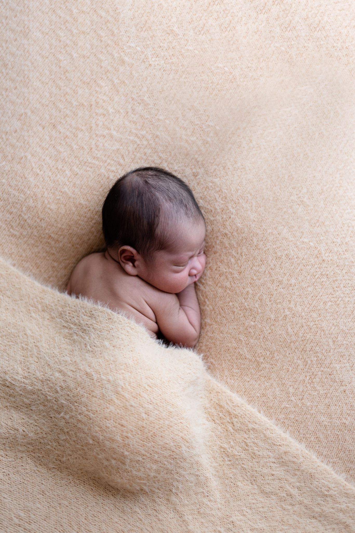Sleeping newborn positioned diagonally on textured beige fabric during a photo shoot.
