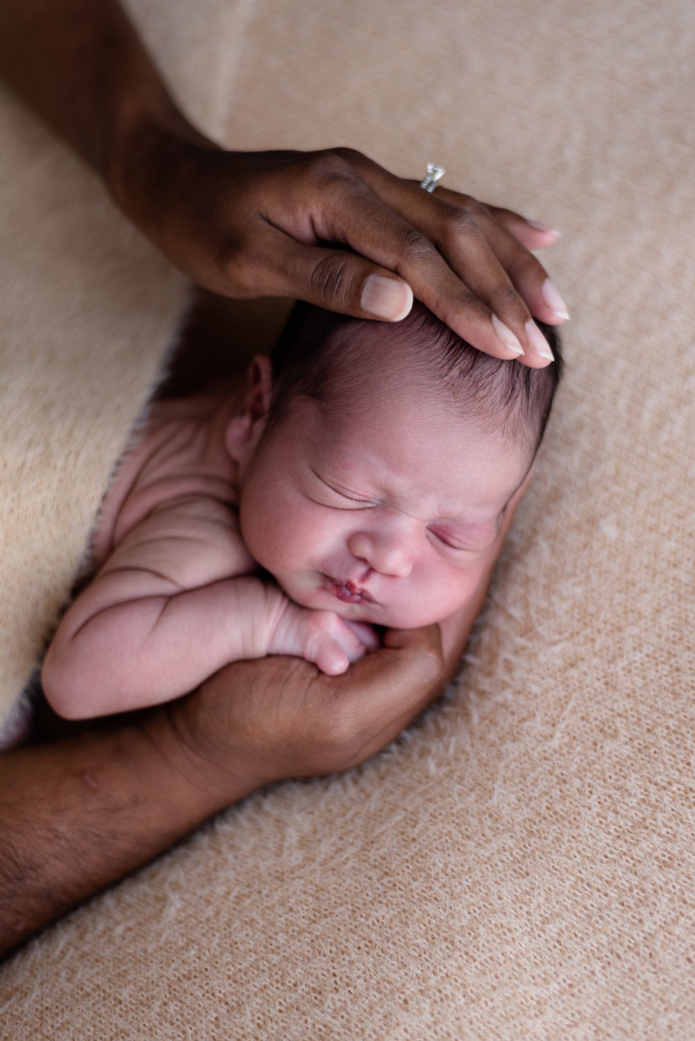 Sleeping newborn cradled gently in caring hands against a beige backdrop.