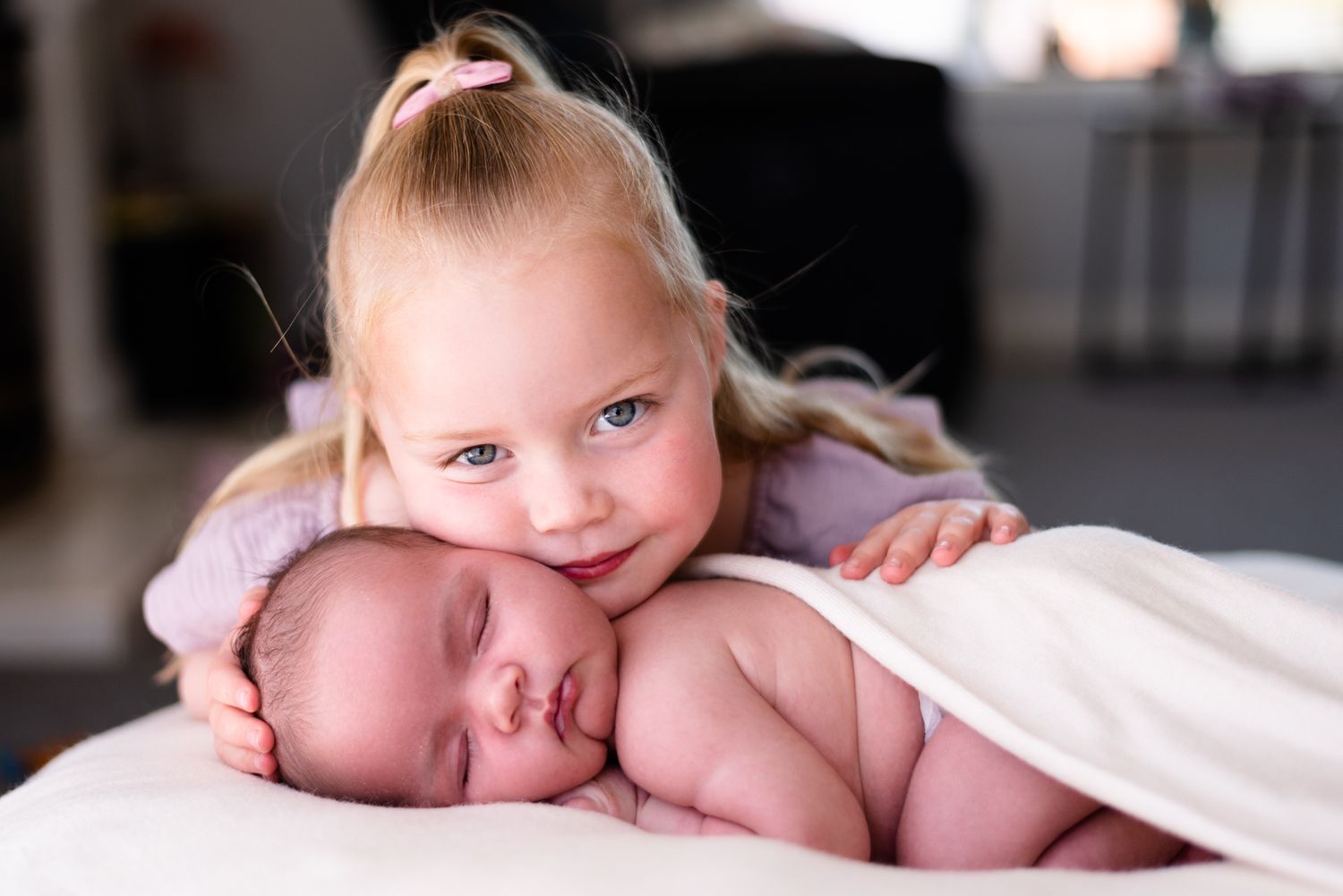 Sweet sibling moment with young child embracing sleeping newborn baby.