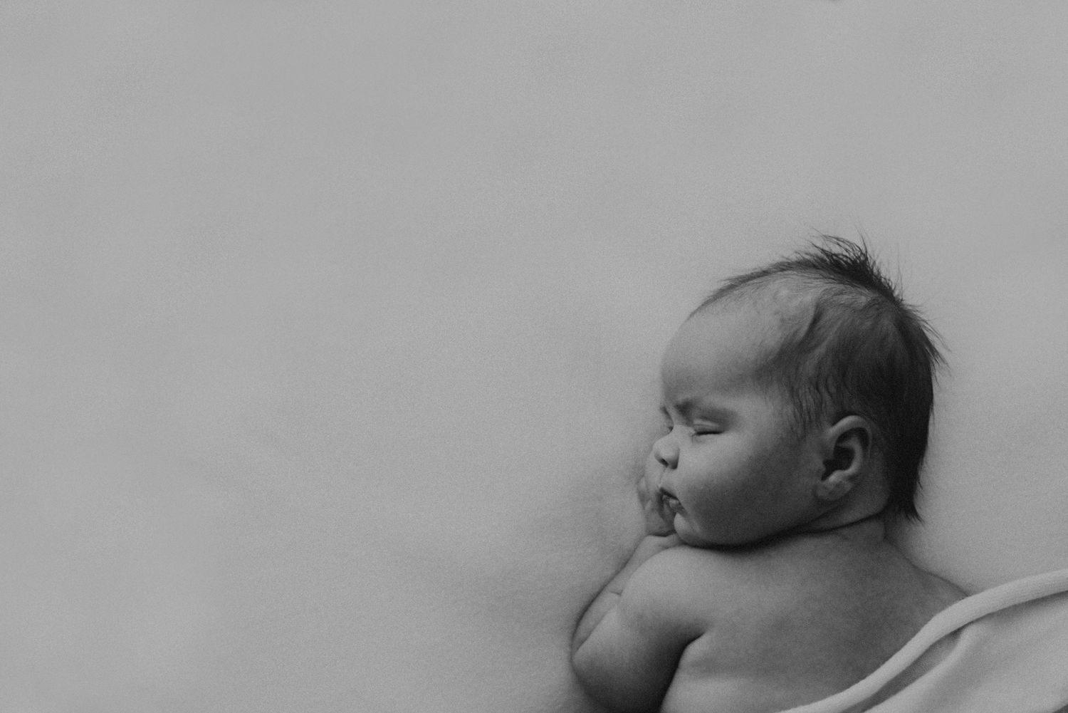 Black and white profile of sleeping newborn against light background.
