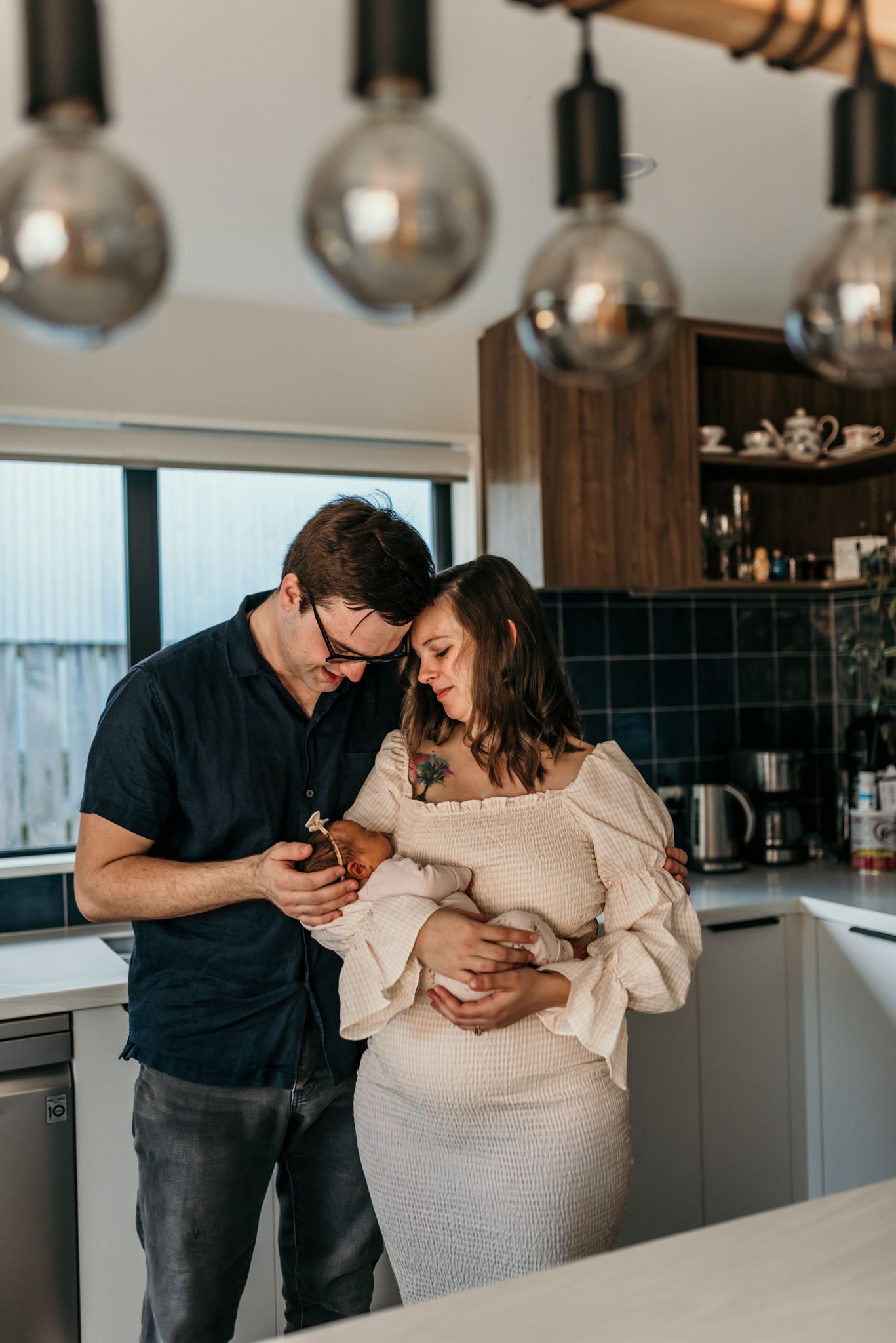 Modern kitchen scene with couple looking at phone under pendant lighting.