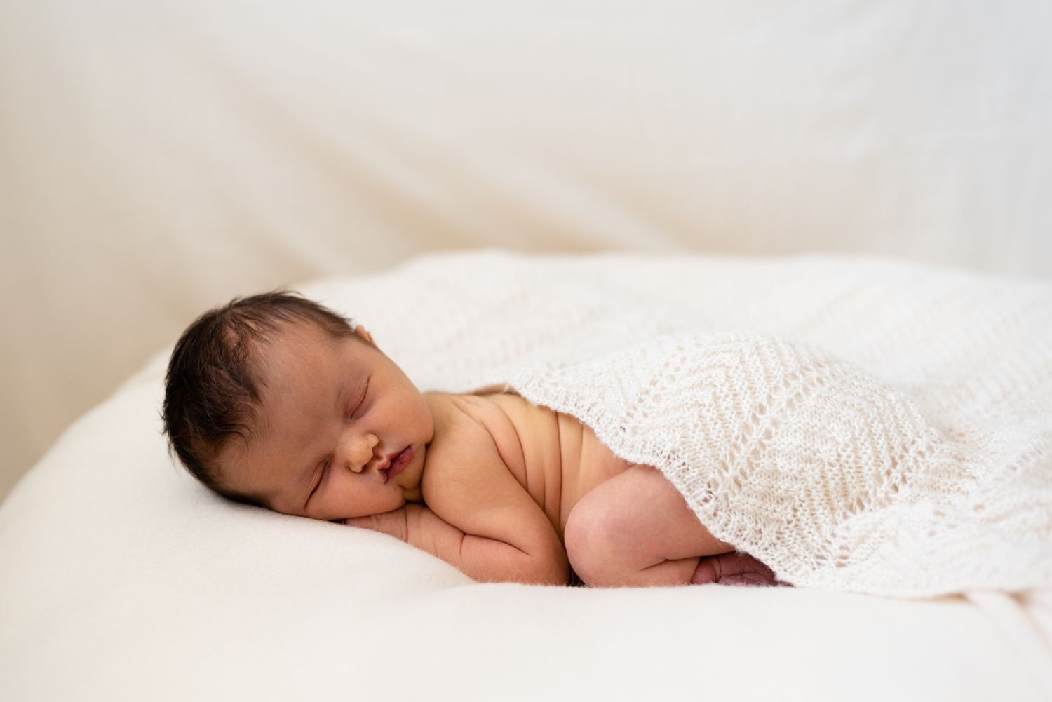 Newborn baby sleeping peacefully under white knitted blanket.