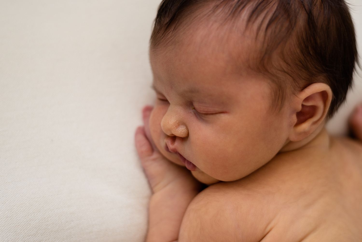 Close-up of peaceful sleeping newborn with hand near face on white background.