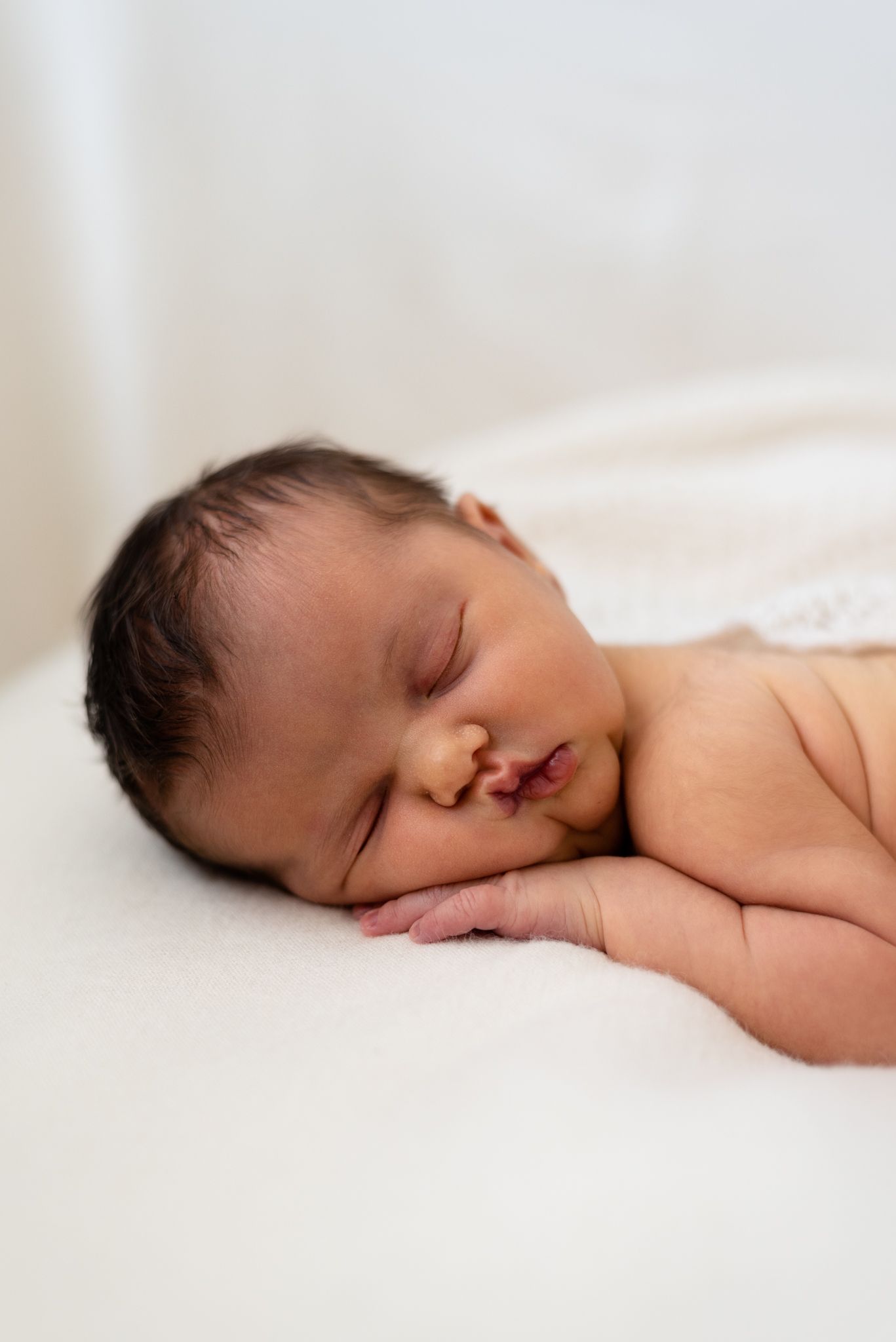 Sleeping newborn baby laying on white bedding in natural light.