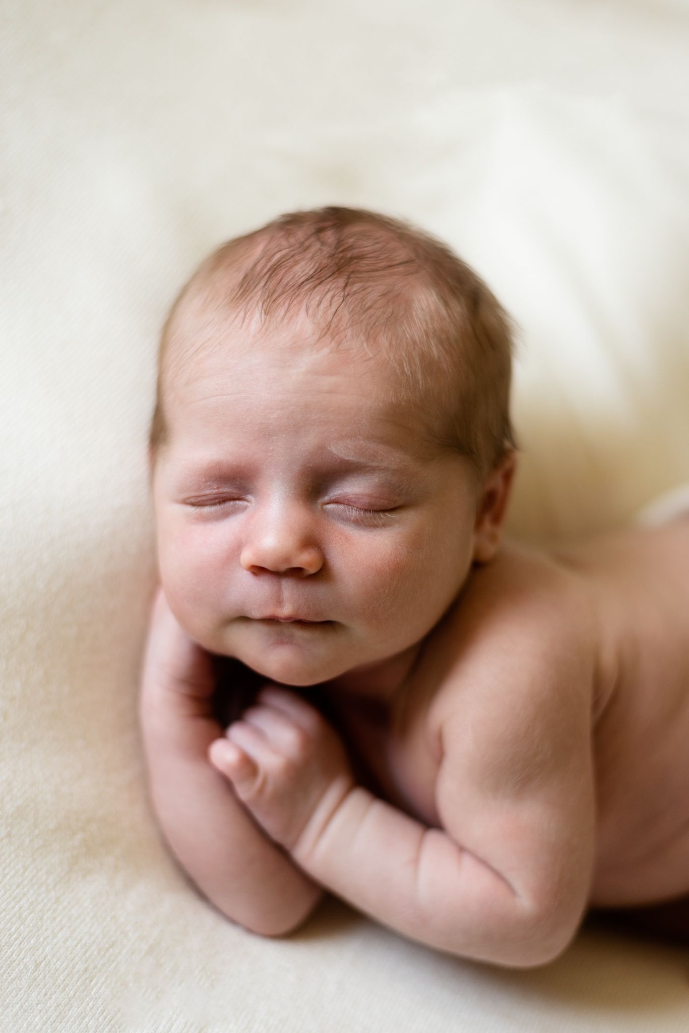 Close-up of sleeping newborn with tiny fists curled under chin.