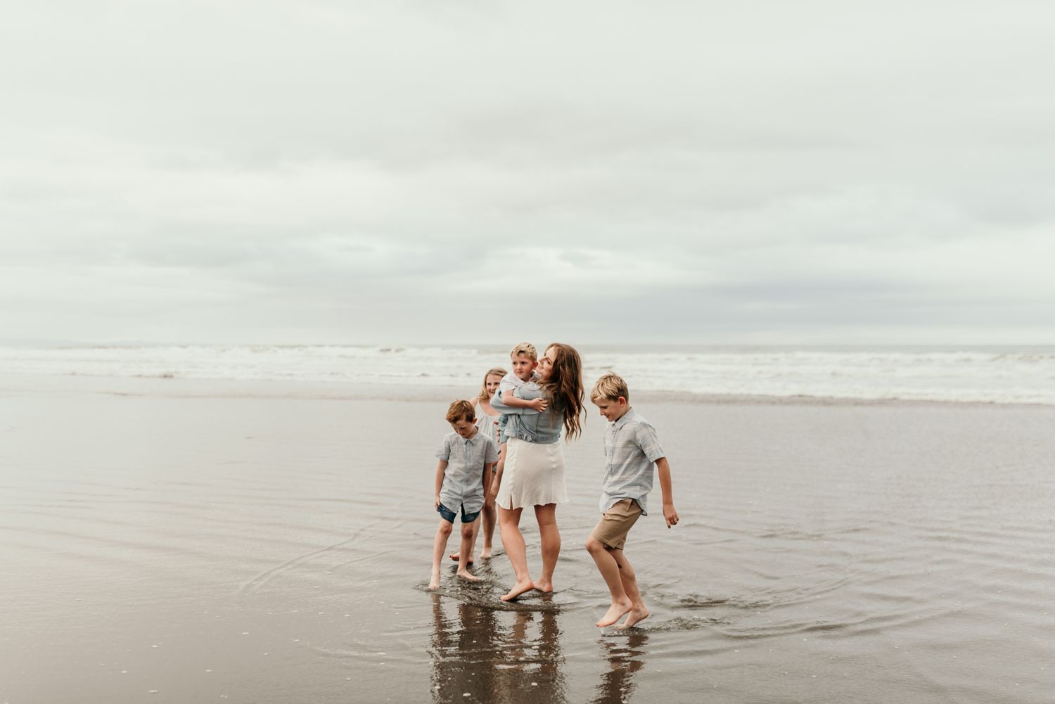 Family playing together in shallow ocean water on an overcast beach day.