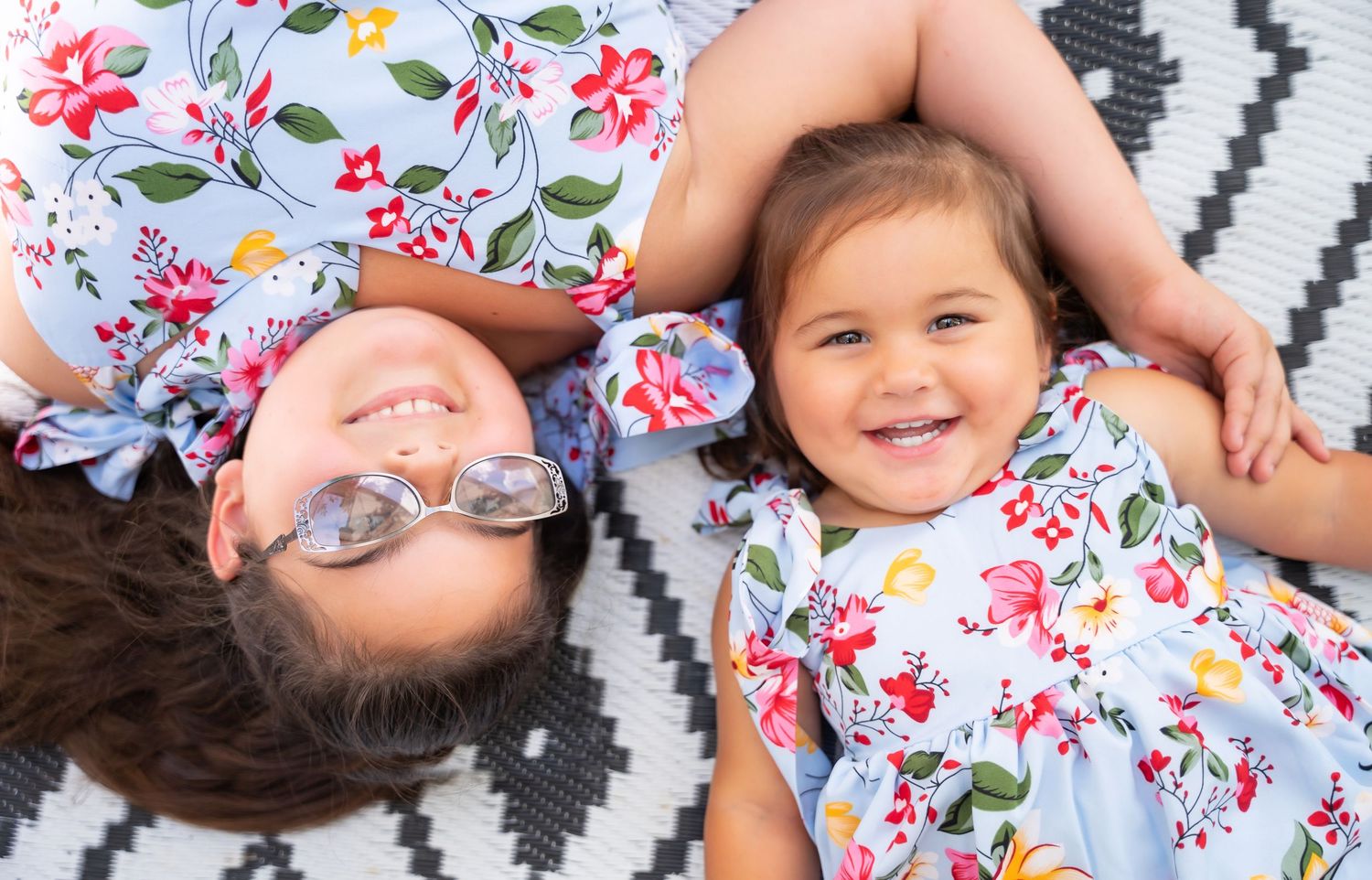 Playful sequence of child in floral dress lying on geometric patterned rug.