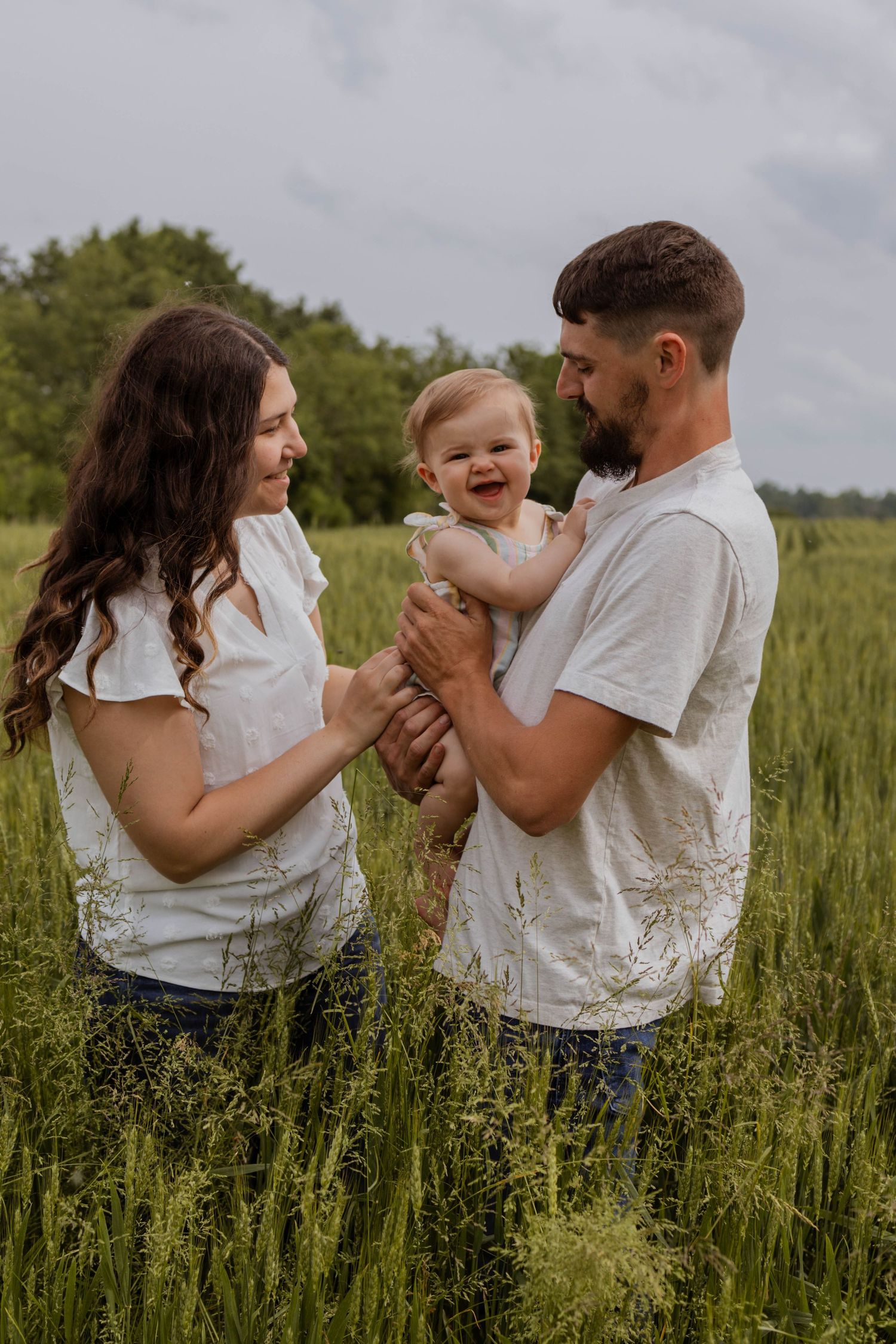 A joyful family plays together in a tall grass field during a summer photoshoot.