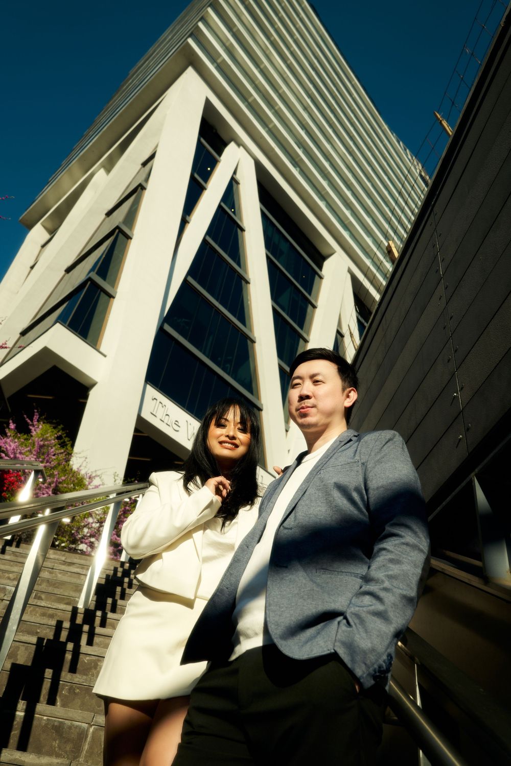A couple poses playfully in front of modern white architecture during an outdoor photoshoot. Engagement  in Williamsburge