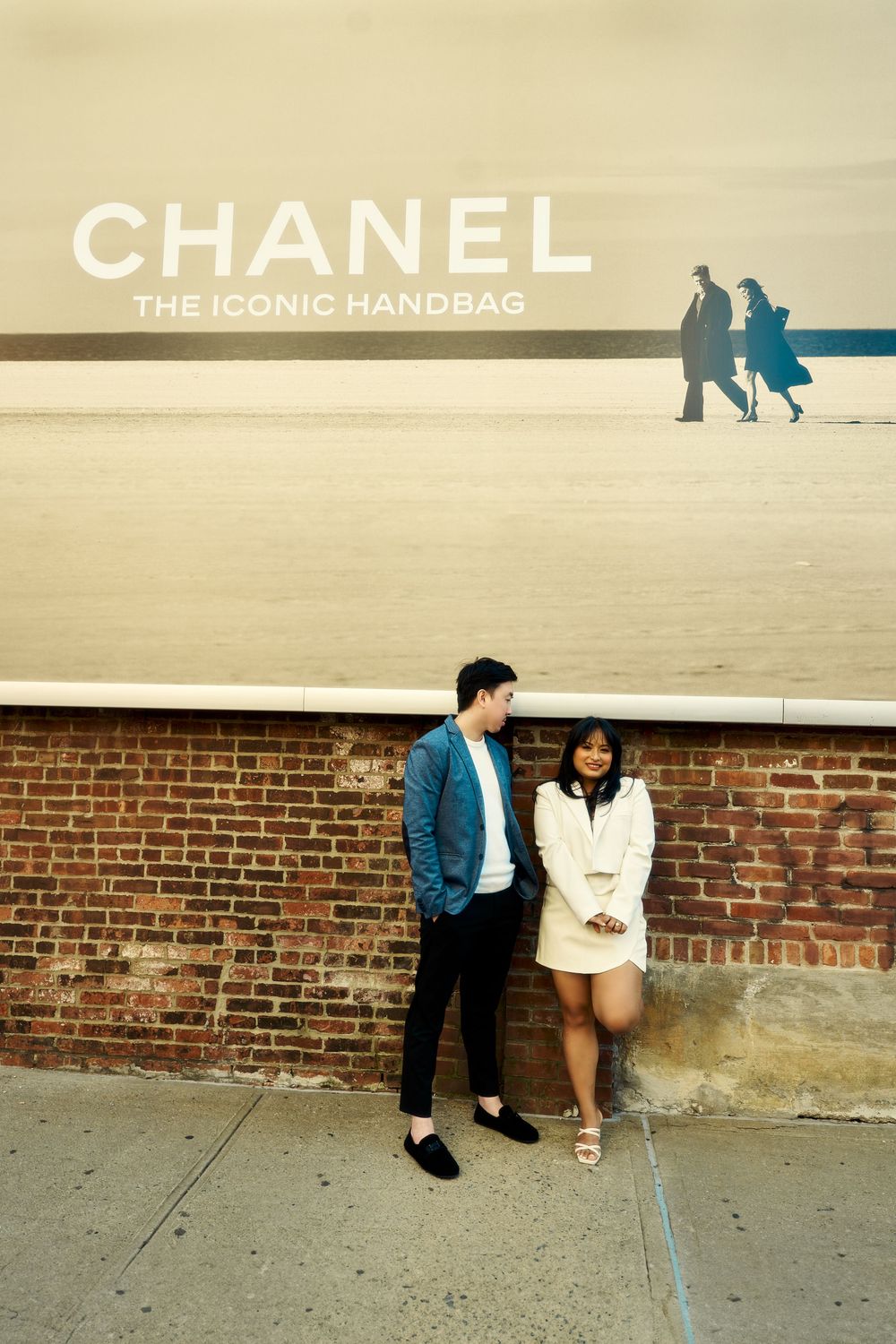 A retro-style urban scene with a Chanel advertisement billboard above a brick wall on a city street. Engagement  in Williamsburge