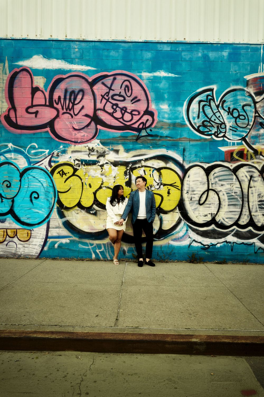 Colorful urban graffiti art spans across a long concrete wall with vibrant blues, yellows and pinks against grey ground. Engagement  in Will