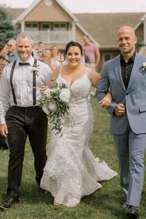 Bride walking down aisle with her two fathers at Whispering Willow summer outdoor wedding in New Brunswick, Canada.