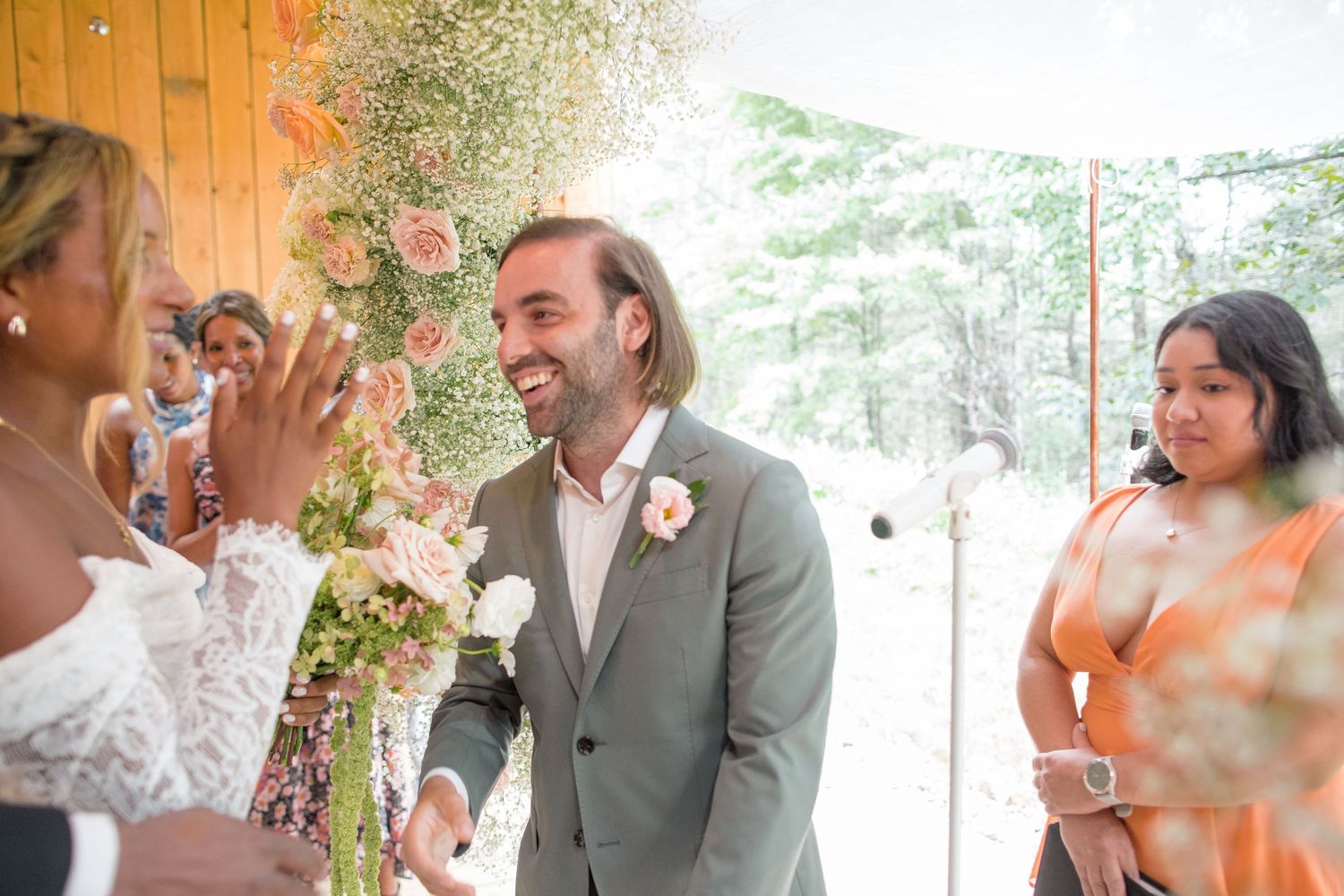 A lively wedding reception celebration under a tent with laughing guests, white decor, and ambient lighting.