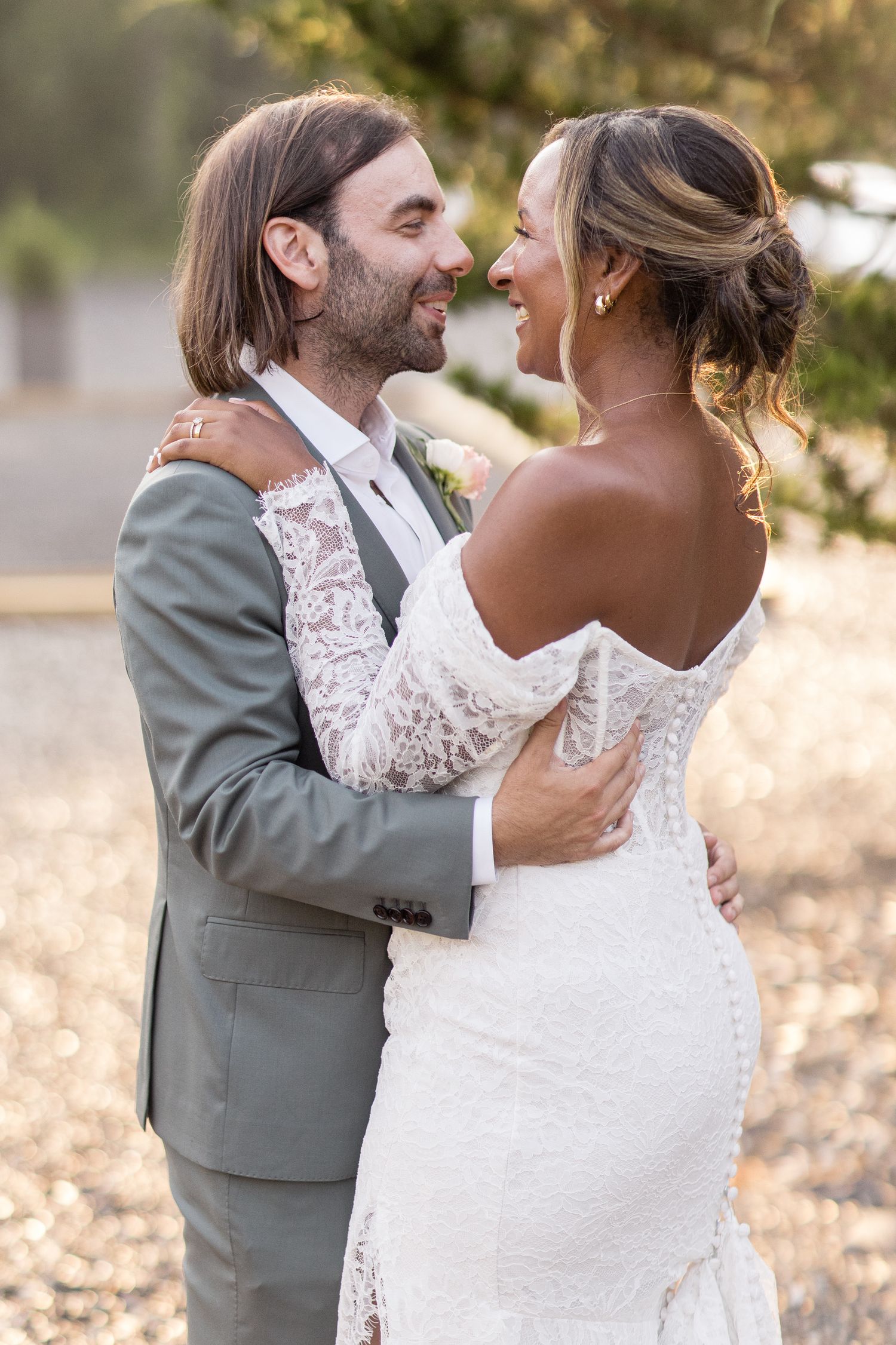 A couple in wedding attire shares a tender moment on a gravel path with twinkle lights glowing softly overhead.