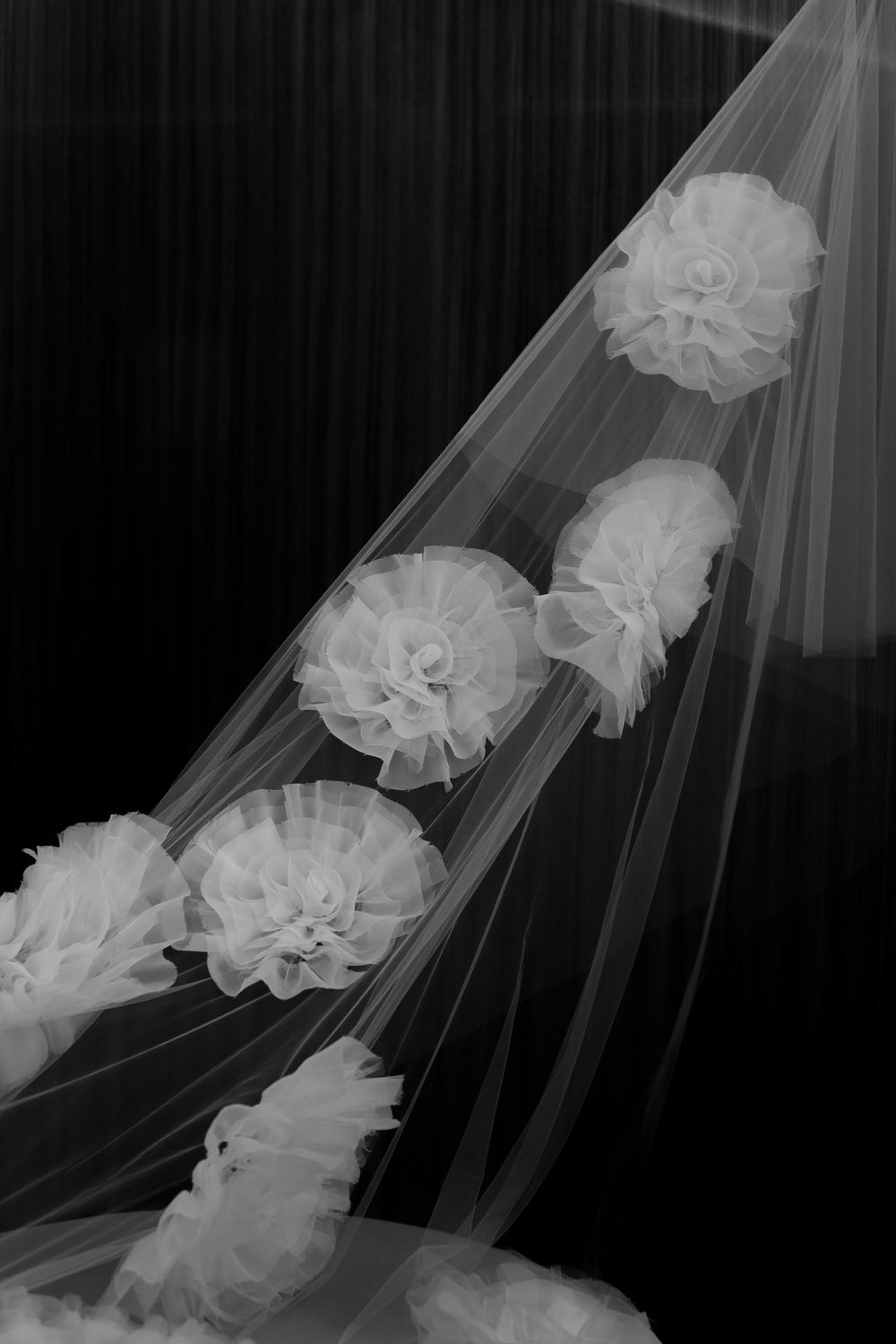 White floral organza accents delicately arranged on sheer tulle veil fabric against dark background.