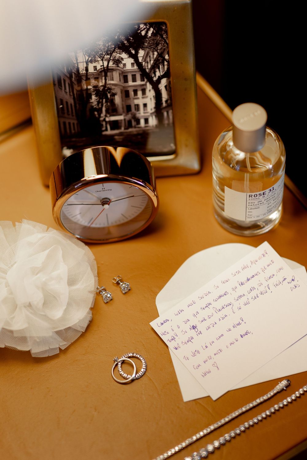Wedding accessories including jewelry, handwritten note, and white decorative pieces displayed on brown surface.