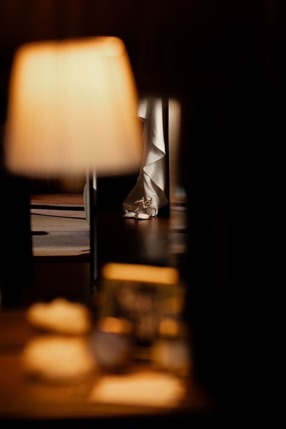 A wedding shoe glimpsed through blurred foreground elements in warm, intimate lighting.