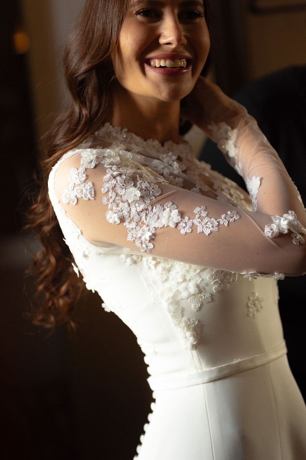 A close-up view of a wedding dress featuring delicate floral lace appliques on sheer fabric against a dark background.