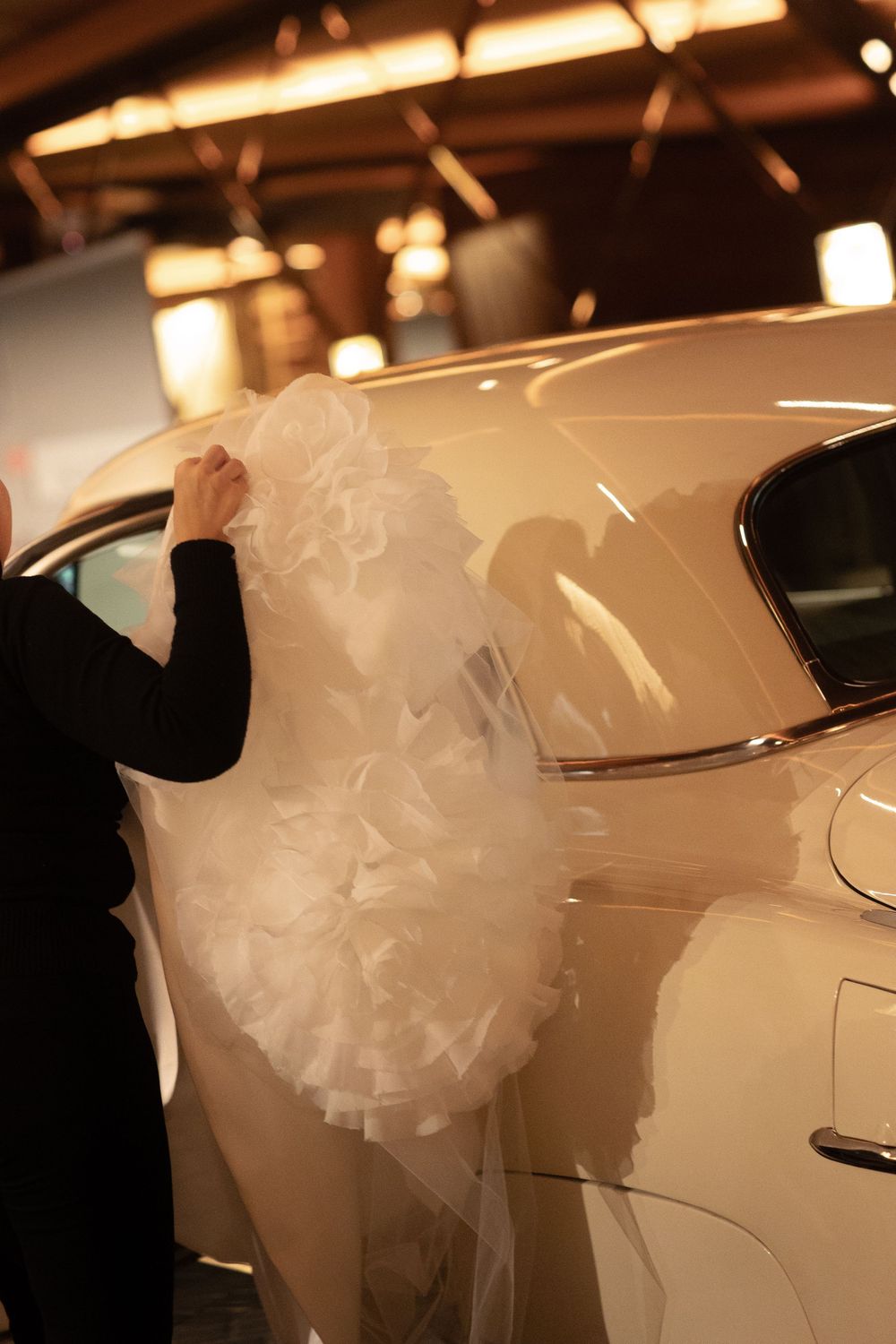Close-up view of white tulle wedding dress fabric and veil details against a car exterior in warm lighting.