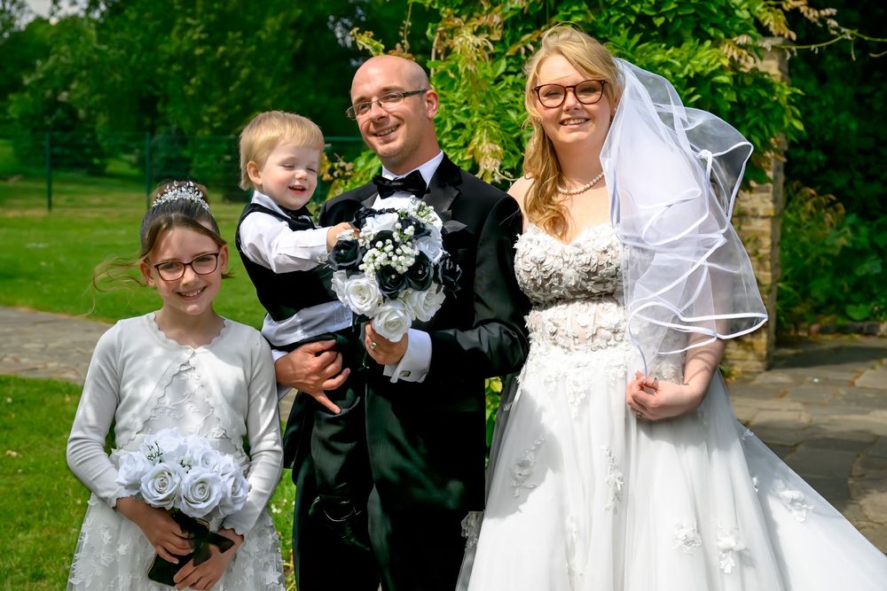 Wedding party posing together outdoors in formal attire surrounded by garden landscaping.
