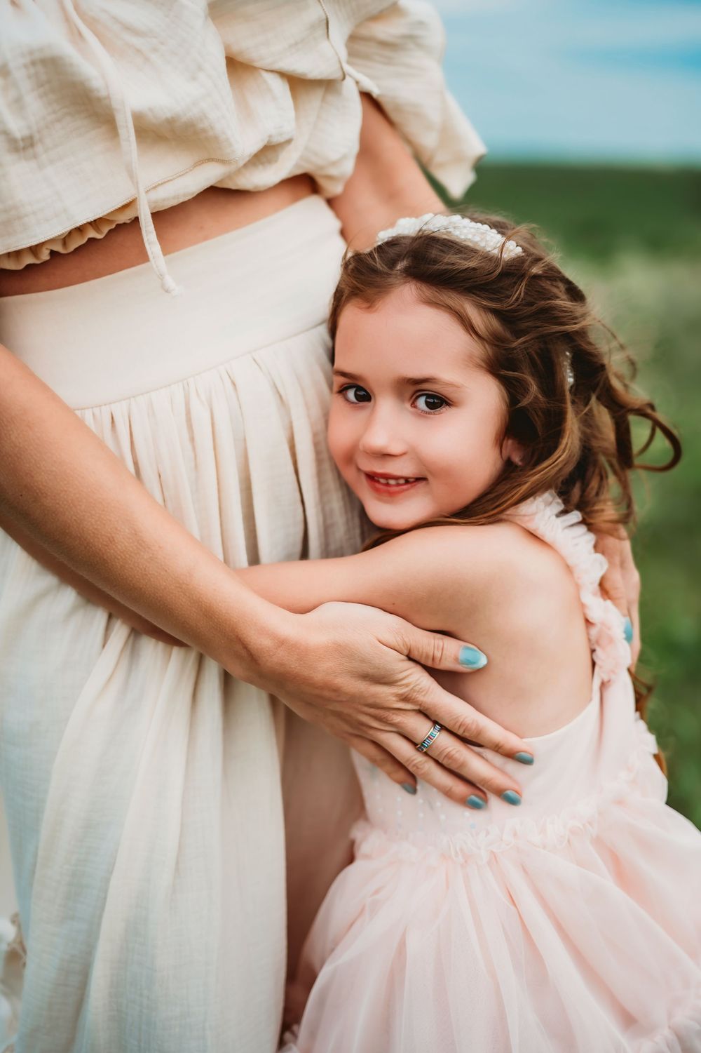 A candid moment captured of hands embracing a child wearing a pink dress in a sun-lit outdoor setting.